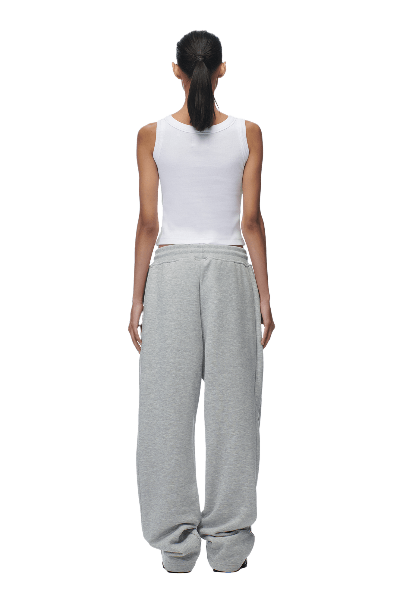 A person with long dark hair in a ponytail models the 6PM OPEN LEG JOGGER GREY, paired with a white sleeveless tank top, standing facing away against a green background.