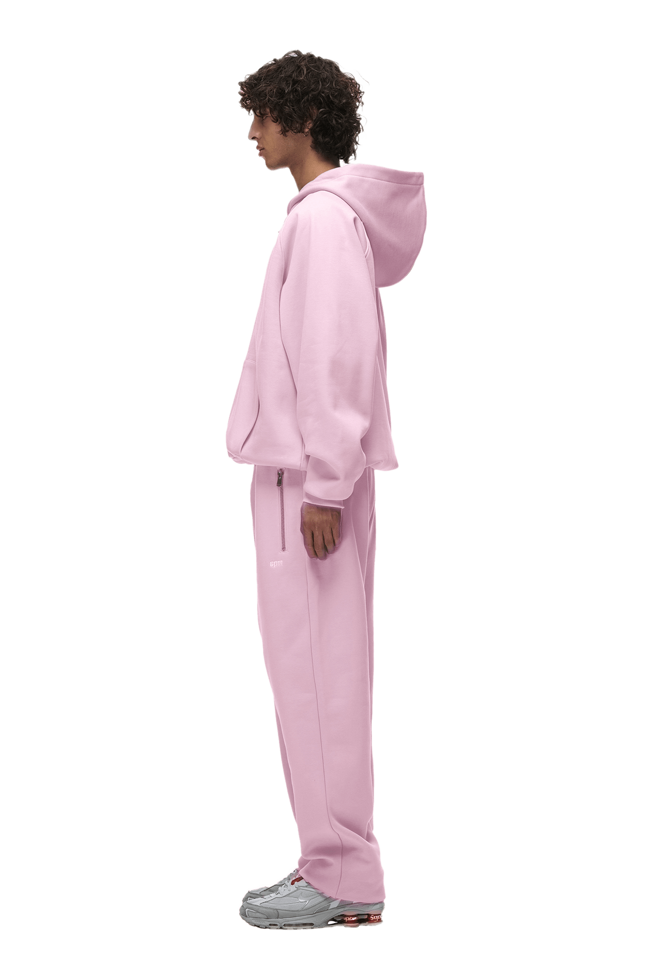 A person in profile models the 6PM HOODIE BABY PINK—a loose-fitting raglan-sleeve hoodie with a kangaroo pocket and matching sweatpants, paired with gray sneakers, on a transparent background—ideal for daily wear.