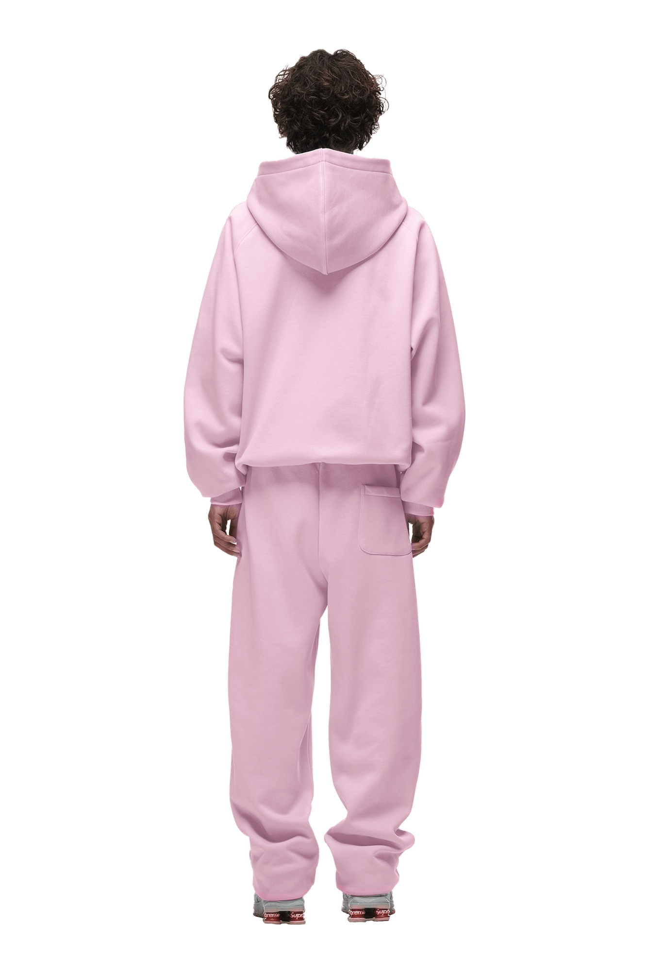 A person with curly hair faces away, modeling the 6PM HOODIE BABY PINK—a light pink raglan-sleeve hoodie with a kangaroo pocket and matching sweatpants. The loose fit is ideal for everyday wear. Background is transparent.
