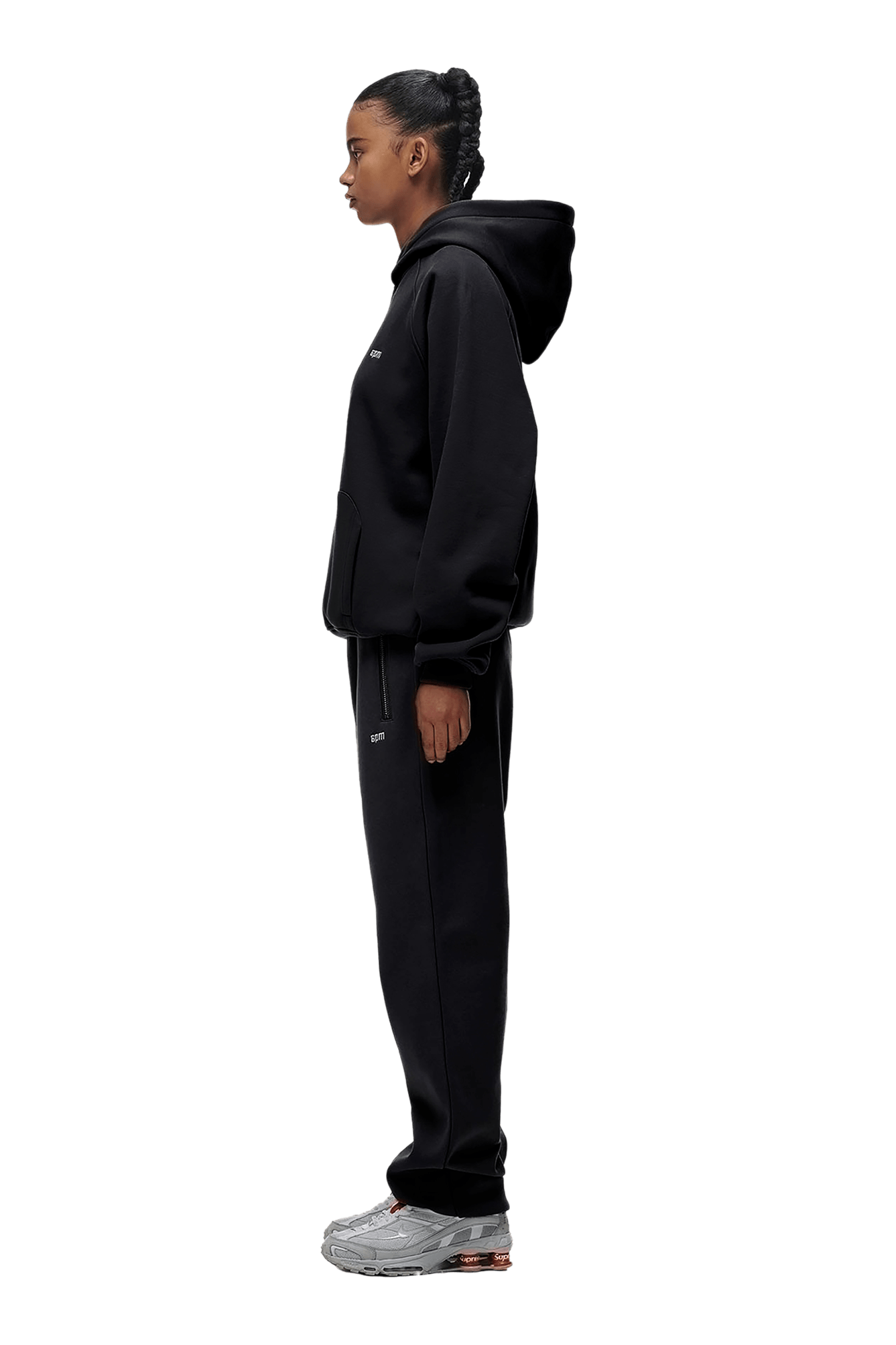 A person stands in profile wearing the HOODIE BLACK, featuring raglan sleeves and a kangaroo pocket, matched with black sweatpants and gray sneakers against a plain green background—ideal for everyday wear.