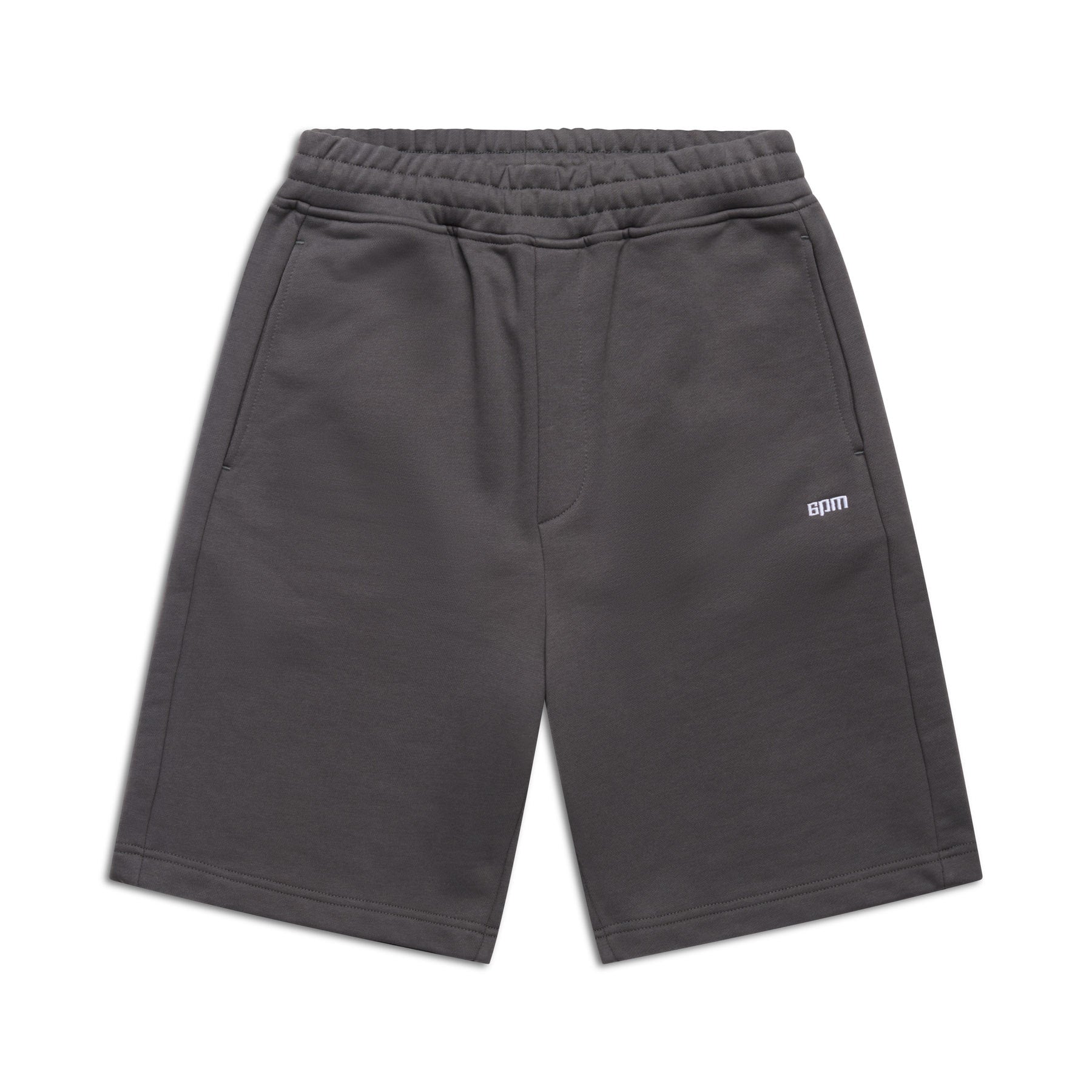 6PM+ SHORTS ANTHRACITE by 6PM: Dark gray athletic shorts with relaxed fit, elastic waistband, side pockets, and a small white 6PM logo on the left leg. Displayed flat on a white background.