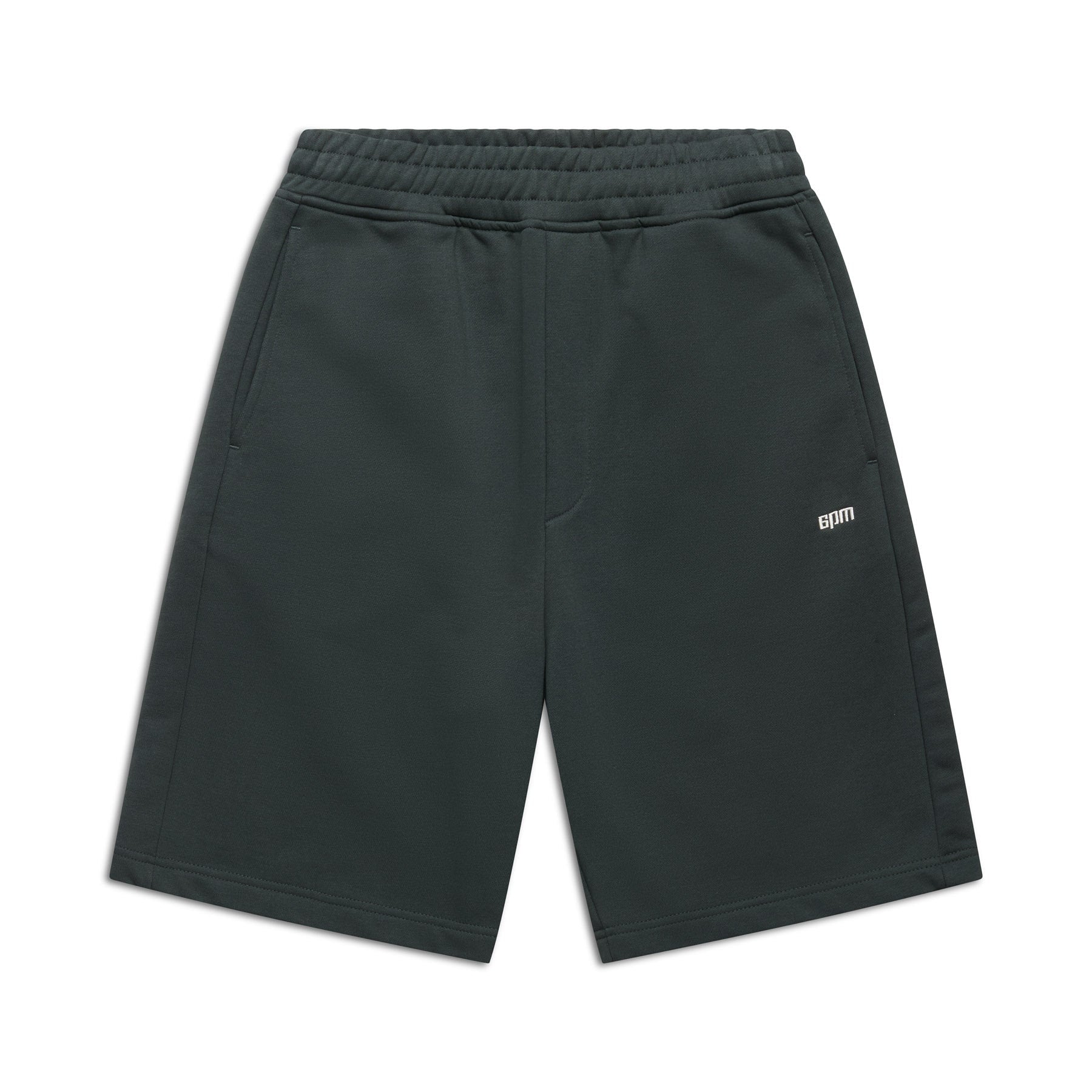 The 6PM+ SHORTS DARK EMERALD by 6PM are knee-length athletic shorts in dark emerald with a soft brushed interior, elastic waistband, side pockets, and a small white BDM logo on the left thigh, shown on a white background.