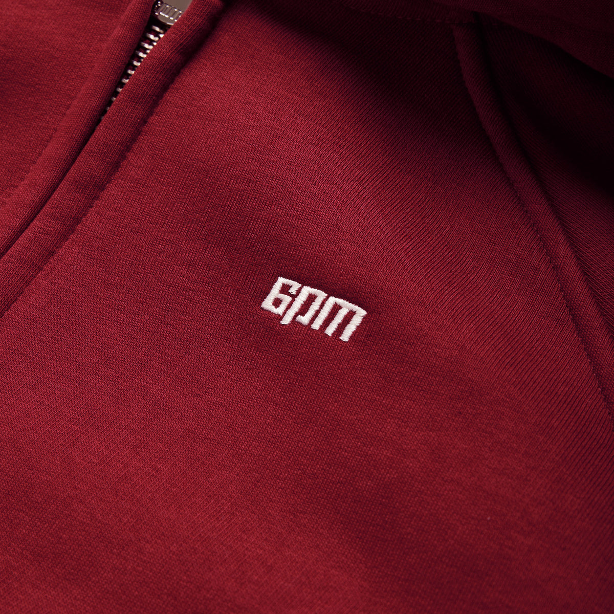 Close-up of the WMNS CROPPED ZIP HOODIE in wine red by 6PM, featuring a visible zipper and white embroidered 6PM branding on the chest.
