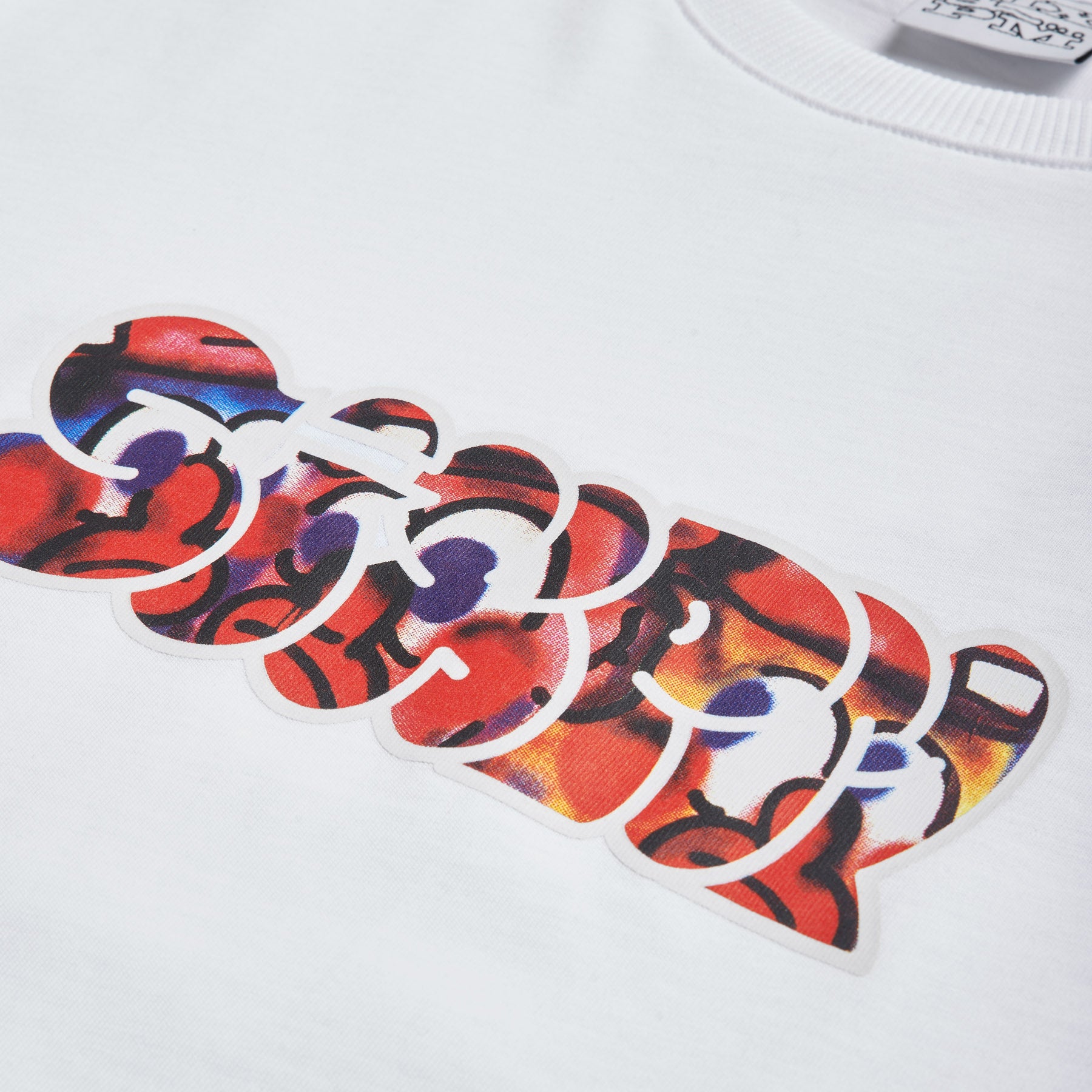 Close-up of the 6PM SLAWN SIGNATURE TEE WHITE, showcasing a vibrant abstract graphic with bold red, blue, and yellow overlapping shapes printed across the chest.