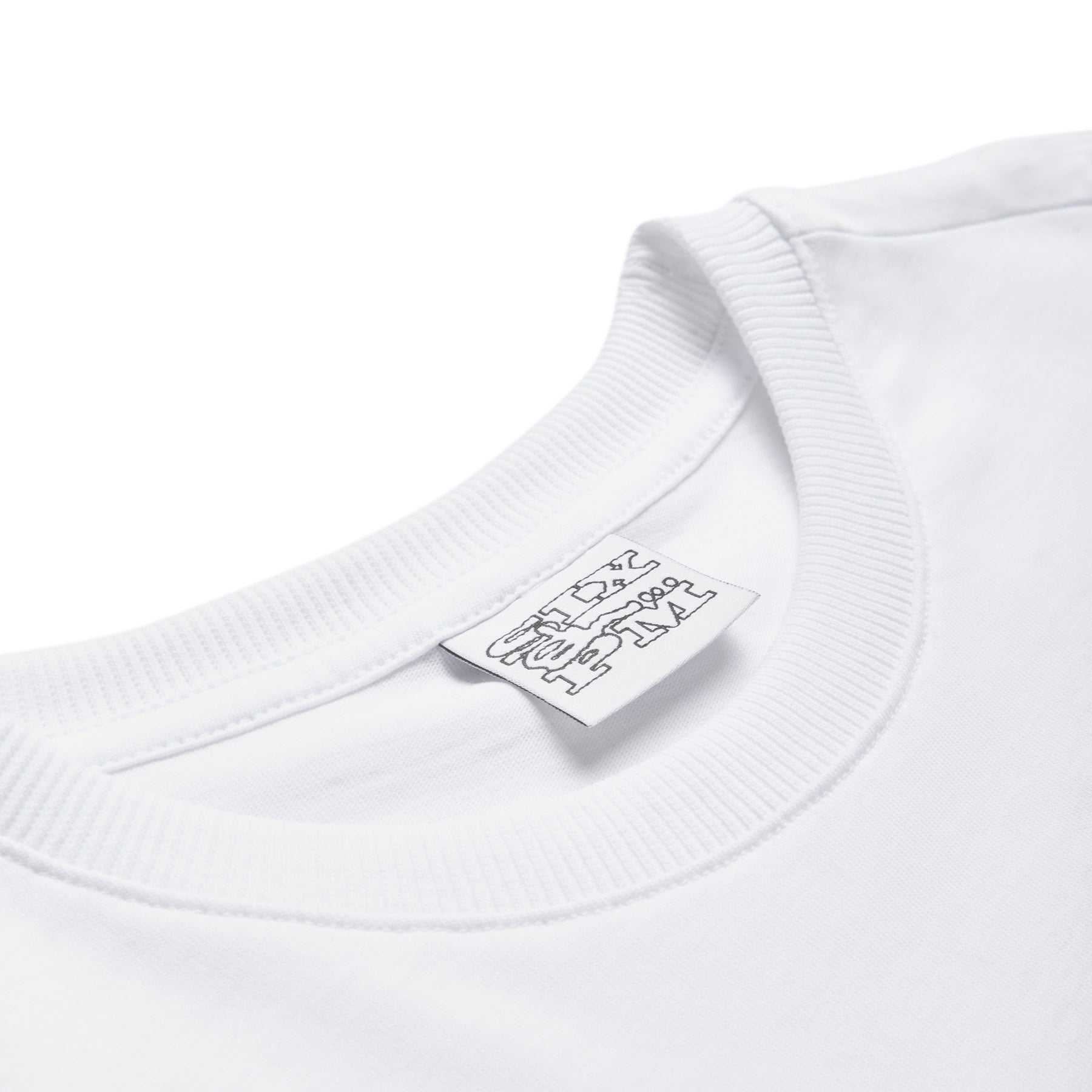 Close-up of the collar and tag on the SLAWN SIGNATURE TEE WHITE by 6PM. The smooth, clean fabric features a ribbed neckline and a white label with black text displaying branding details.