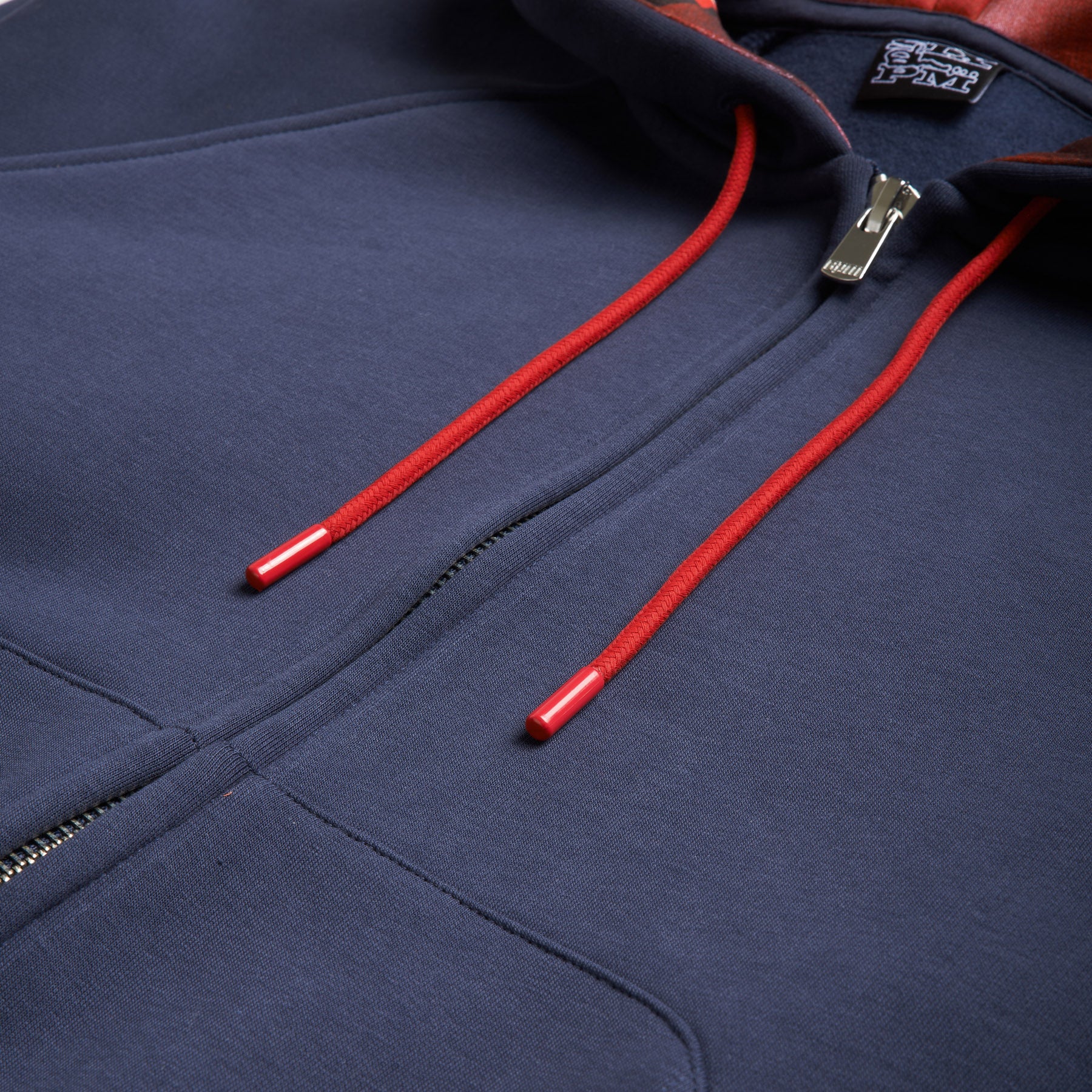 Close-up of the SLAWN ZIP HOODIE by 6PM in navy blue, featuring red drawstrings with metal tips. The zipper is partially open, revealing the garments soft, thick fabric.