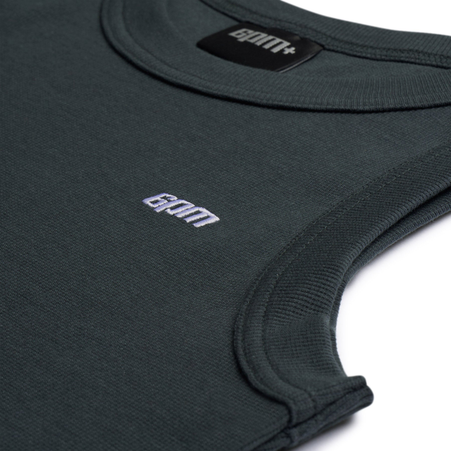 Close-up of the 6PM TANK TOP DARK EMERALD featuring ribbed edges, a small white gom logo embroidered on the front, and a black inside-collar tag with the gom+ logo.