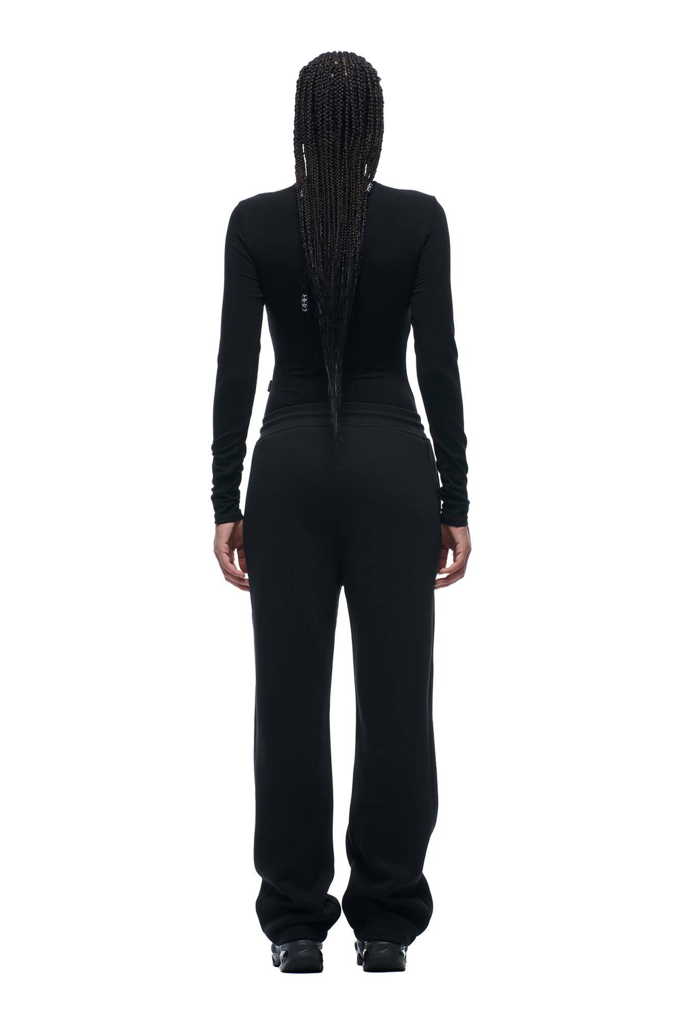 A person with long, braided hair is standing and facing away, wearing the 6PM WMNS LONGSLEEVE BLACK top paired with loose black pants and black shoes.