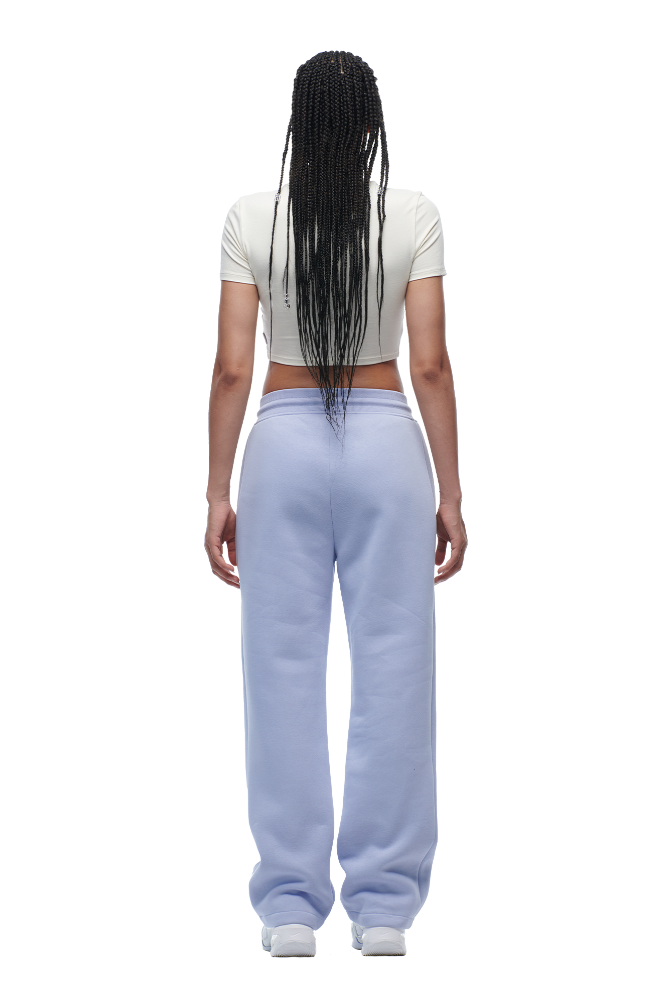 A person with long braided hair faces away, wearing the 6PM WMNS CROPPED T-SHIRT OFF-WHITE, light blue sweatpants, and white sneakers.