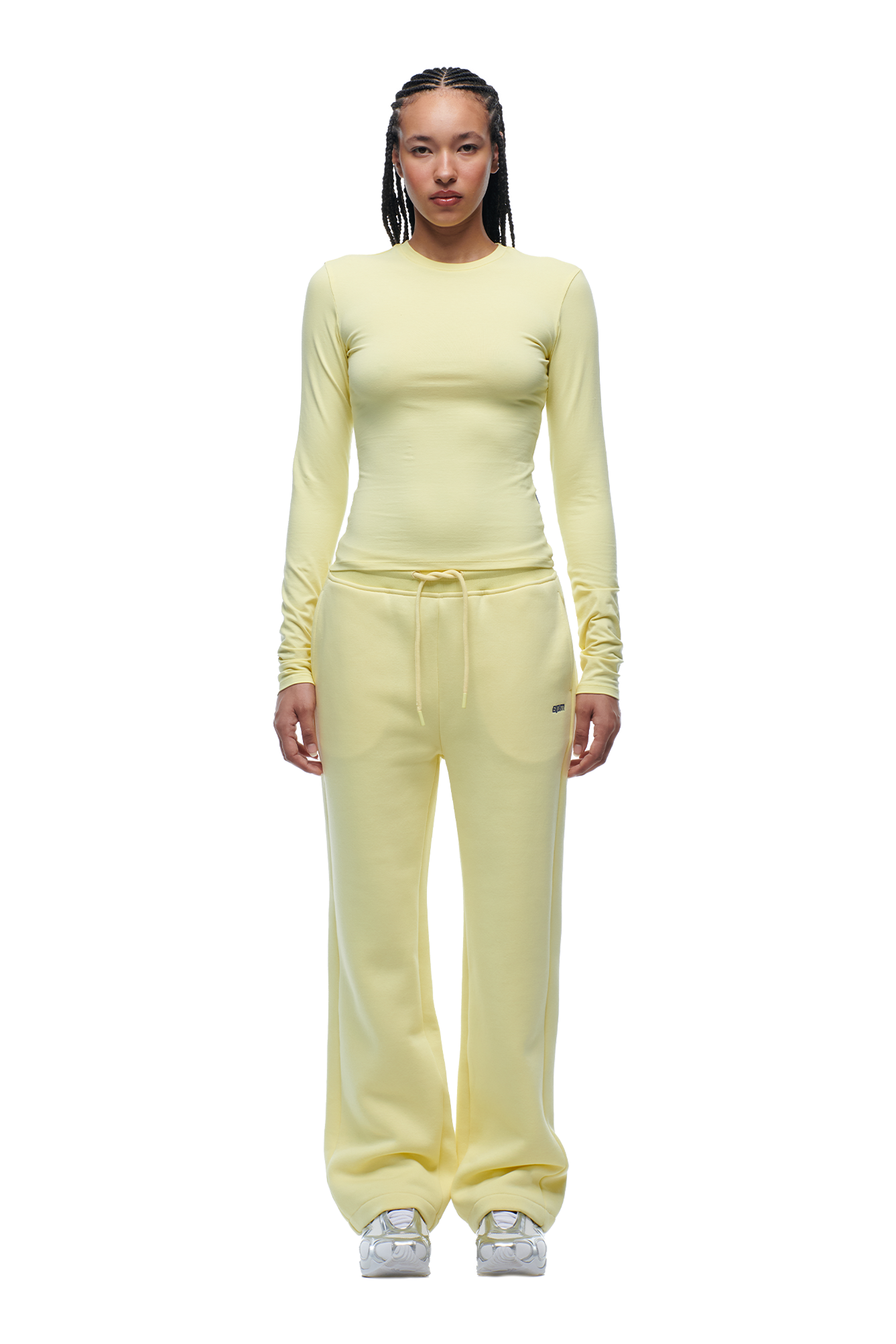 A person stands facing forward in a 6PM WMNS LONGSLEEVE BUTTERCREAM top and matching loose yellow sweatpants with drawstrings, paired with white sneakers. The background is plain white.
