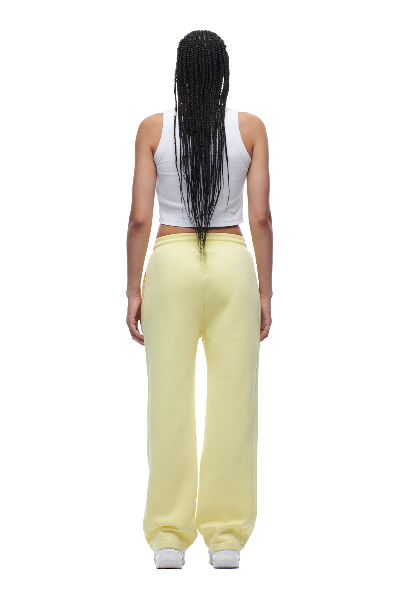 A person with long braided hair wears the 6PM WMNS OPEN LEG BUTTERCREAM sweatpants and a white sleeveless top, standing with their back to the camera against a white background.