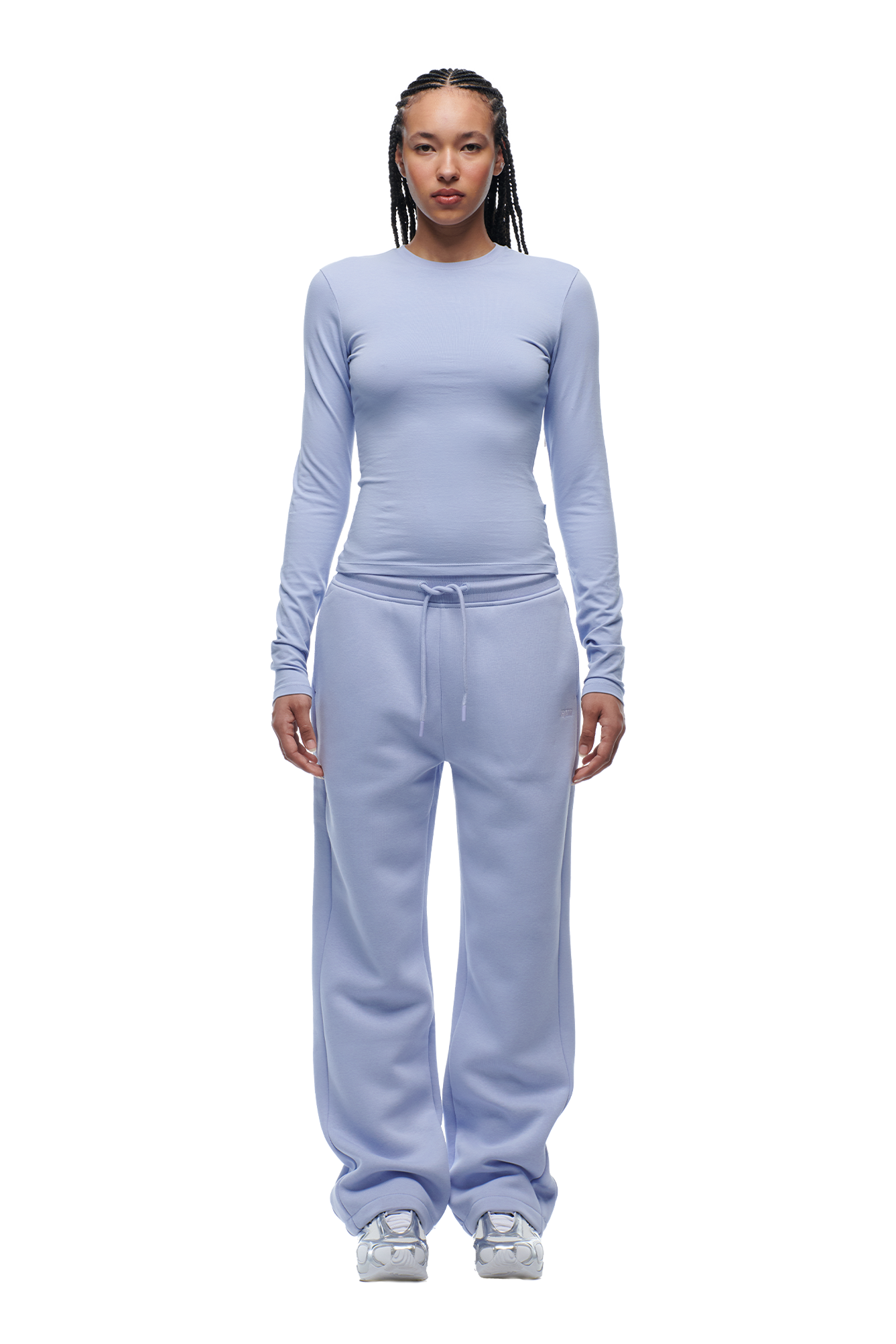 A person with braided hair stands facing forward, wearing the 6PM WMNS LONGSLEEVE SOFT VIOLET top and matching sweatpants with white sneakers.