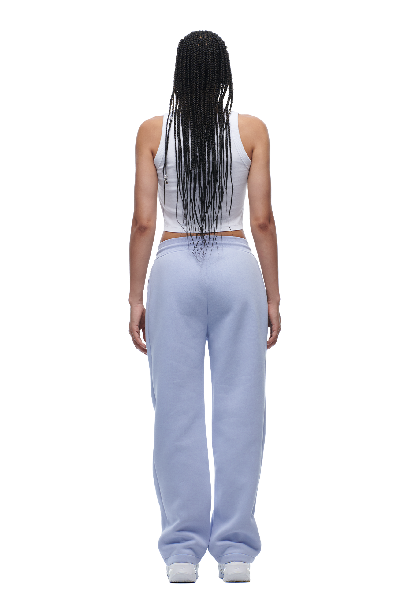 A woman with long braided hair, wearing the 6PM WMNS OPEN LEG SOFT VIOLET sweatpants and a white sleeveless top, stands facing away from the camera against a white background.