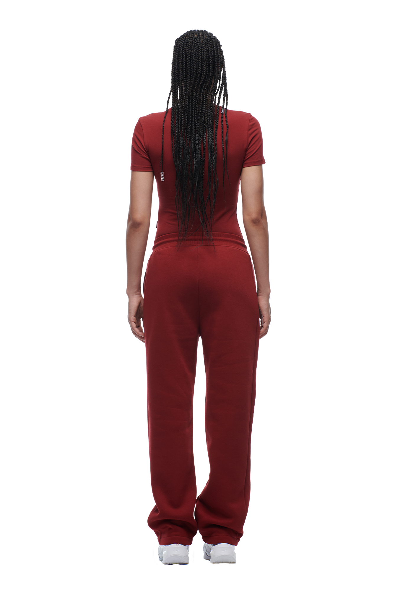 A woman with long braided hair faces away from the camera, wearing a fitted 6PM WMNS T-SHIRT WINE RED and matching sweatpants, paired with white sneakers.