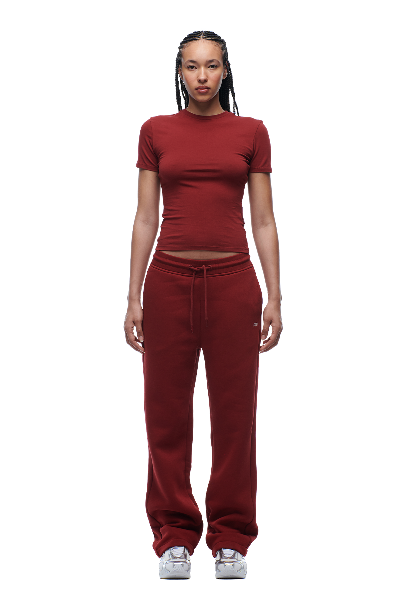 A person with braided hair and a neutral expression faces forward, wearing the 6PM WMNS T-SHIRT WINE RED, matching maroon sweatpants with a drawstring, and white sneakers against a plain white background.