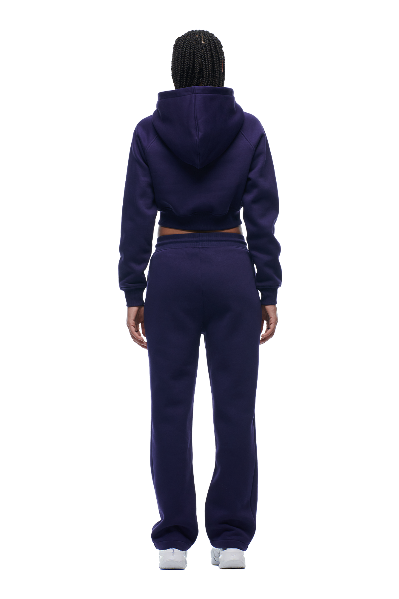 A person with braided hair, seen from behind, wears the 6PM WMNS Cropped Zip Hoodie in Orbit Blue with matching sweatpants and white sneakers.