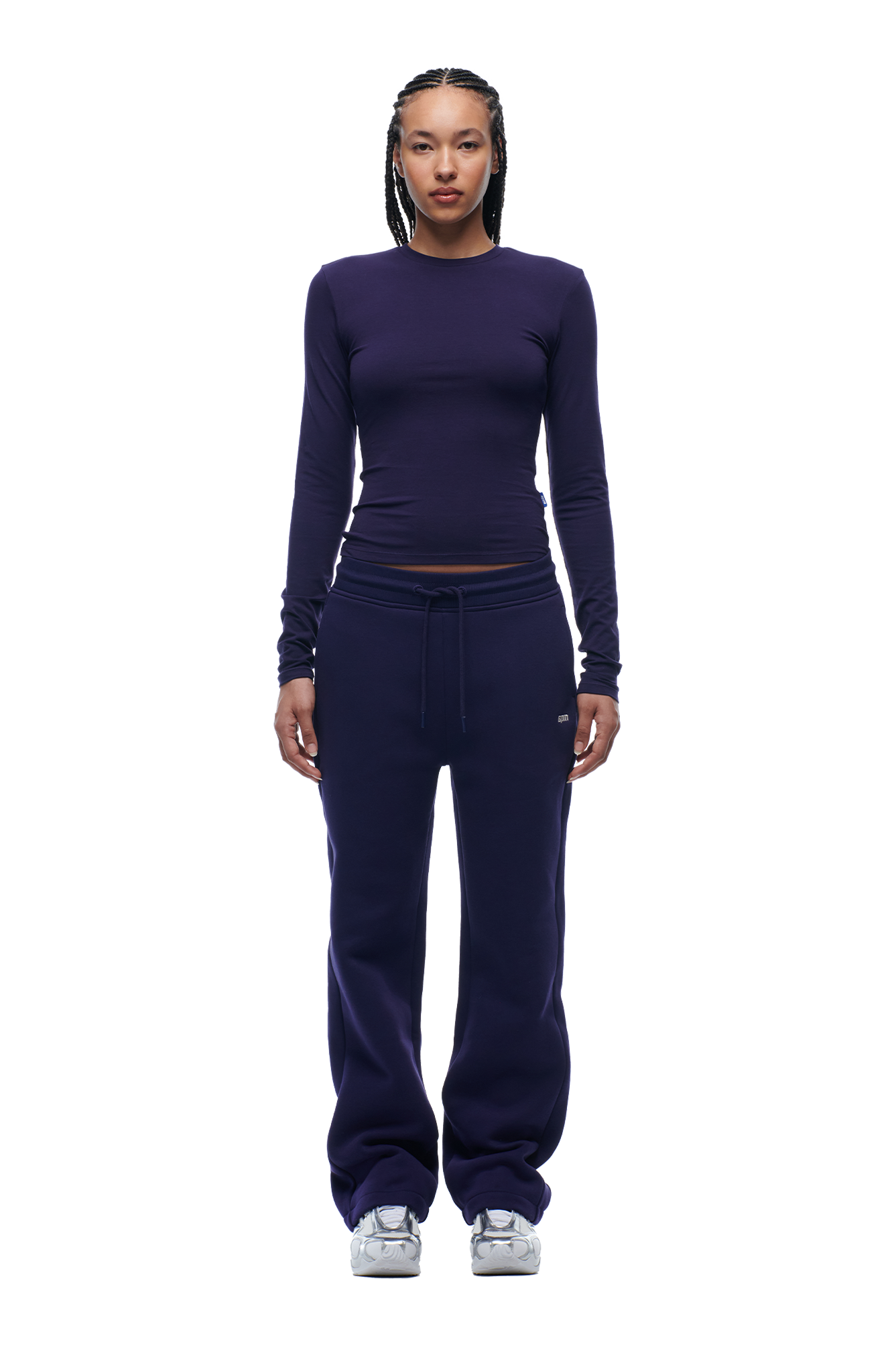 A woman with braided hair and a neutral expression faces forward, wearing the 6PM WMNS LONGSLEEVE ORBIT BLUE top, matching drawstring sweatpants, and white sneakers.