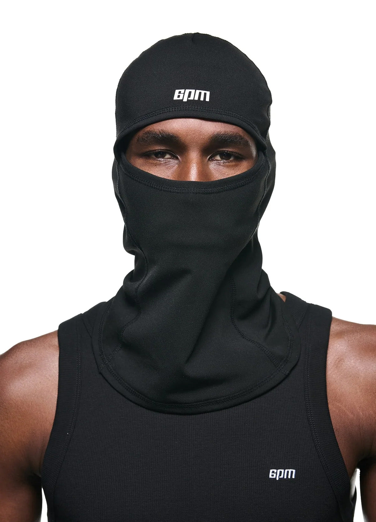 A person wears the TECH BALACLAVA BLACK and a black sleeveless shirt, both by 6PM with white logos, against a plain white background. Only their eyes and part of their forehead are visible.