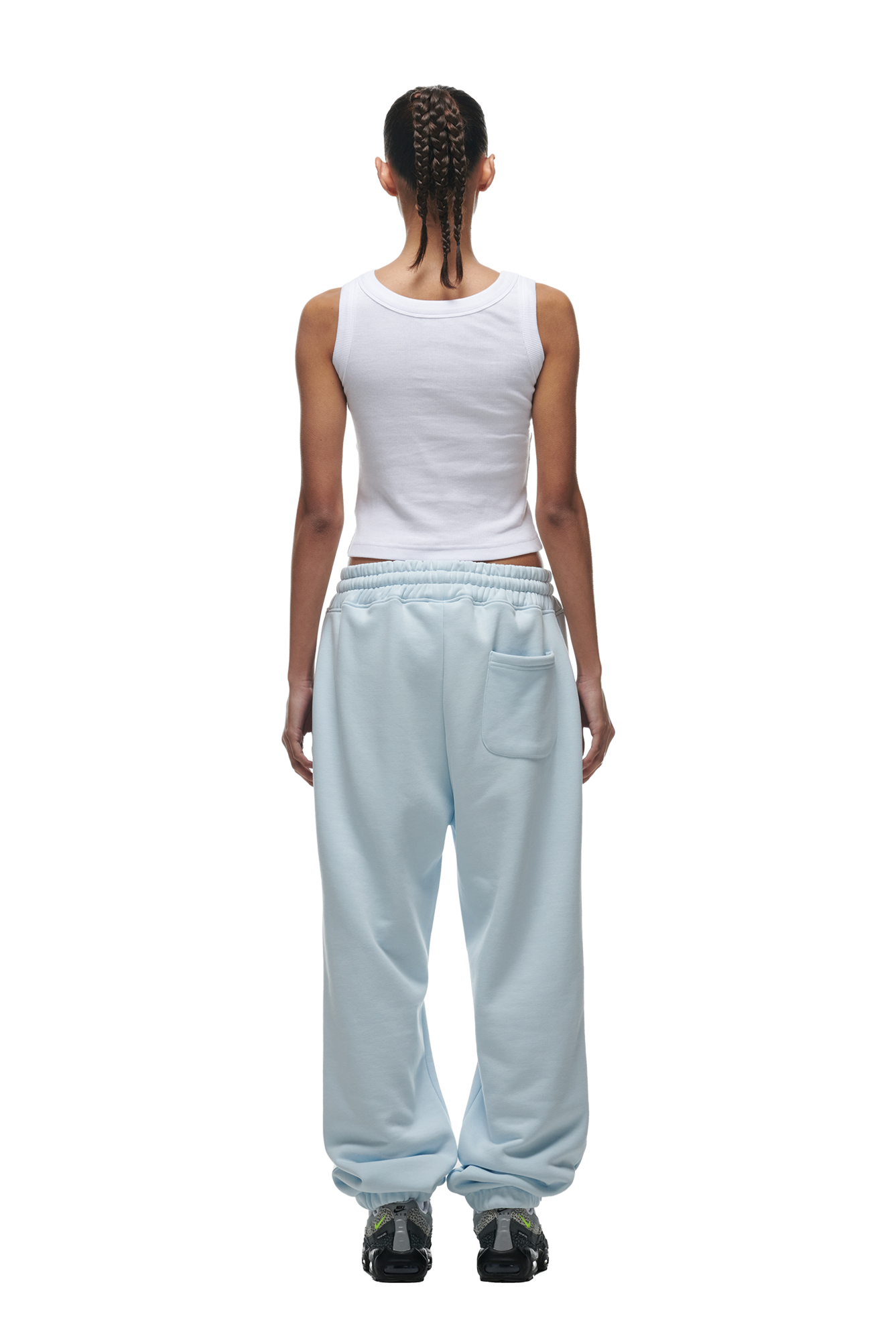 A person with braided hair, dressed in a white tank top and 6PM’s CUFF JOGGER ICE BLUE sweatpants, stands with their back to the camera against a white background.