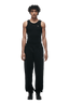 A young man with curly hair faces forward, wearing CUFF JOGGER BLACK sweatpants with cuffed leg openings, a black sleeveless top, and black sneakers against a plain background.