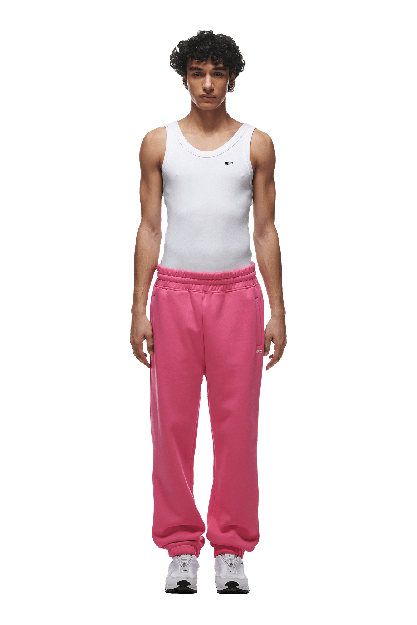 A man stands facing forward against a plain green background, wearing 6PM’s CUFF JOGGER HOT PINK sweatpants, a white sleeveless tank top, and white sneakers.