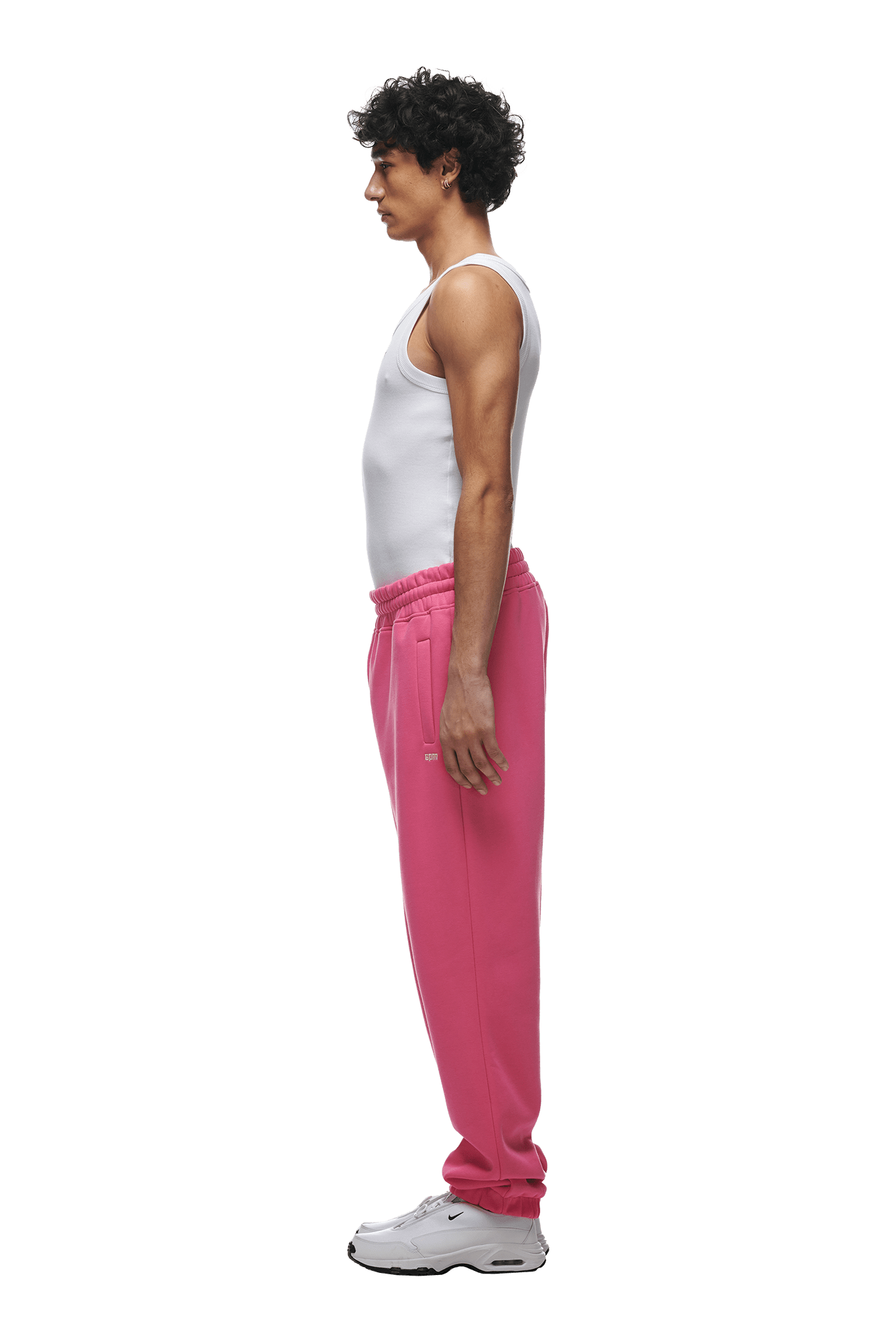 A person in profile faces left, wearing a white tank top, 6PM CUFF JOGGER HOT PINK sweatpants with cuffed leg openings, and white sneakers, set against a transparent background.