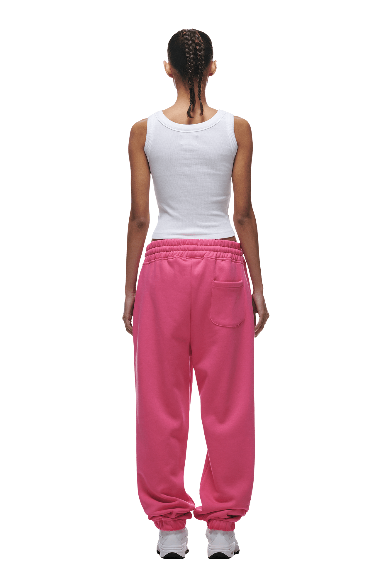 A person with braided hair faces away, wearing a white tank top, 6PM CUFF JOGGER HOT PINK classic fit sweatpants with cuffed leg openings, and white sneakers against a plain background.