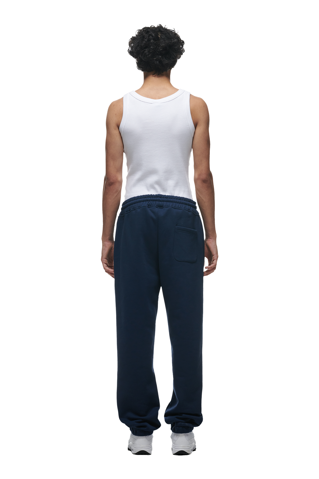 A person with curly hair wears a white tank top, 6PM CUFF JOGGER NAVY sweatpants, and white sneakers, standing with their back to the camera against a white background.