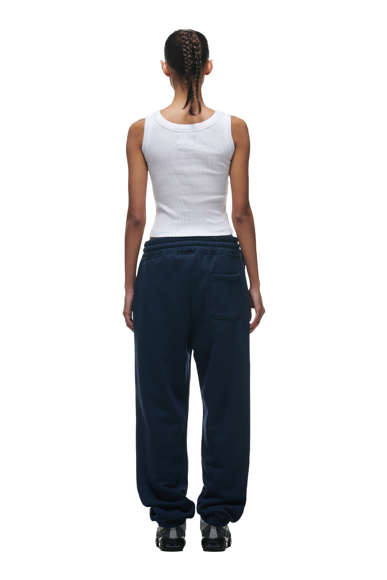 A person with braided hair faces away, wearing a white sleeveless ribbed tank top and 6PM CUFF JOGGER NAVY sweatpants featuring pockets and cuffed legs, paired with black shoes.