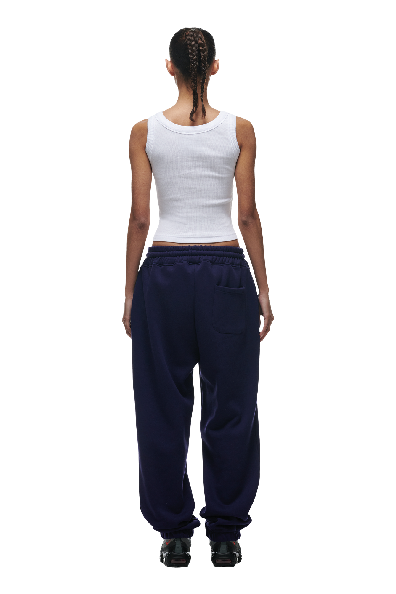 A woman with tightly braided hair stands with her back to the camera, wearing a white sleeveless tank top and 6PM CUFF JOGGER ORBIT BLUE sweatpants featuring classic fit and cuffed leg openings.