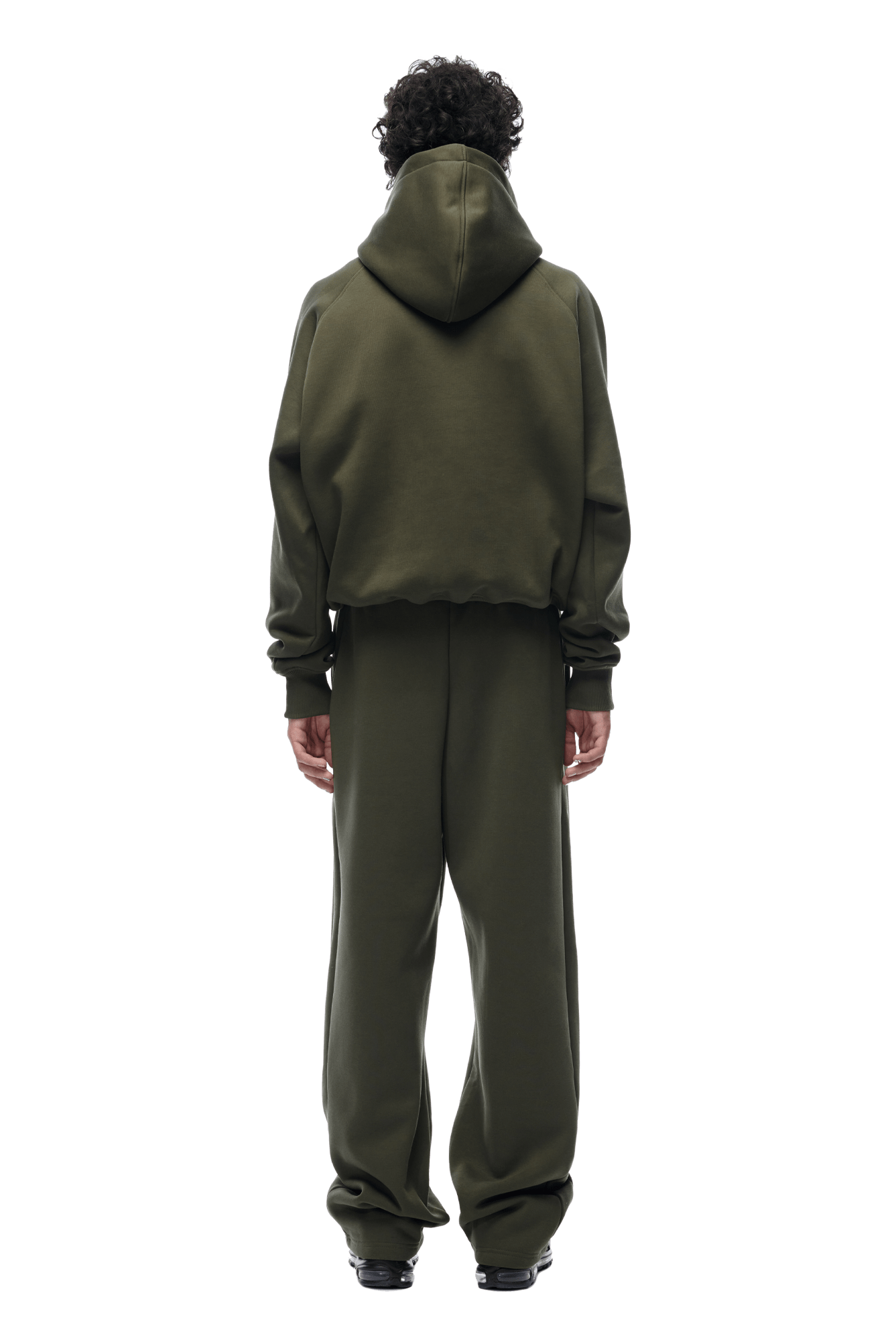 A person with curly hair faces away, wearing the 6PM HOODIE FOREST NIGHT—a relaxed raglan-sleeved olive hoodie with matching sweatpants and black shoes—ideal for everyday wear, shown against a transparent background.