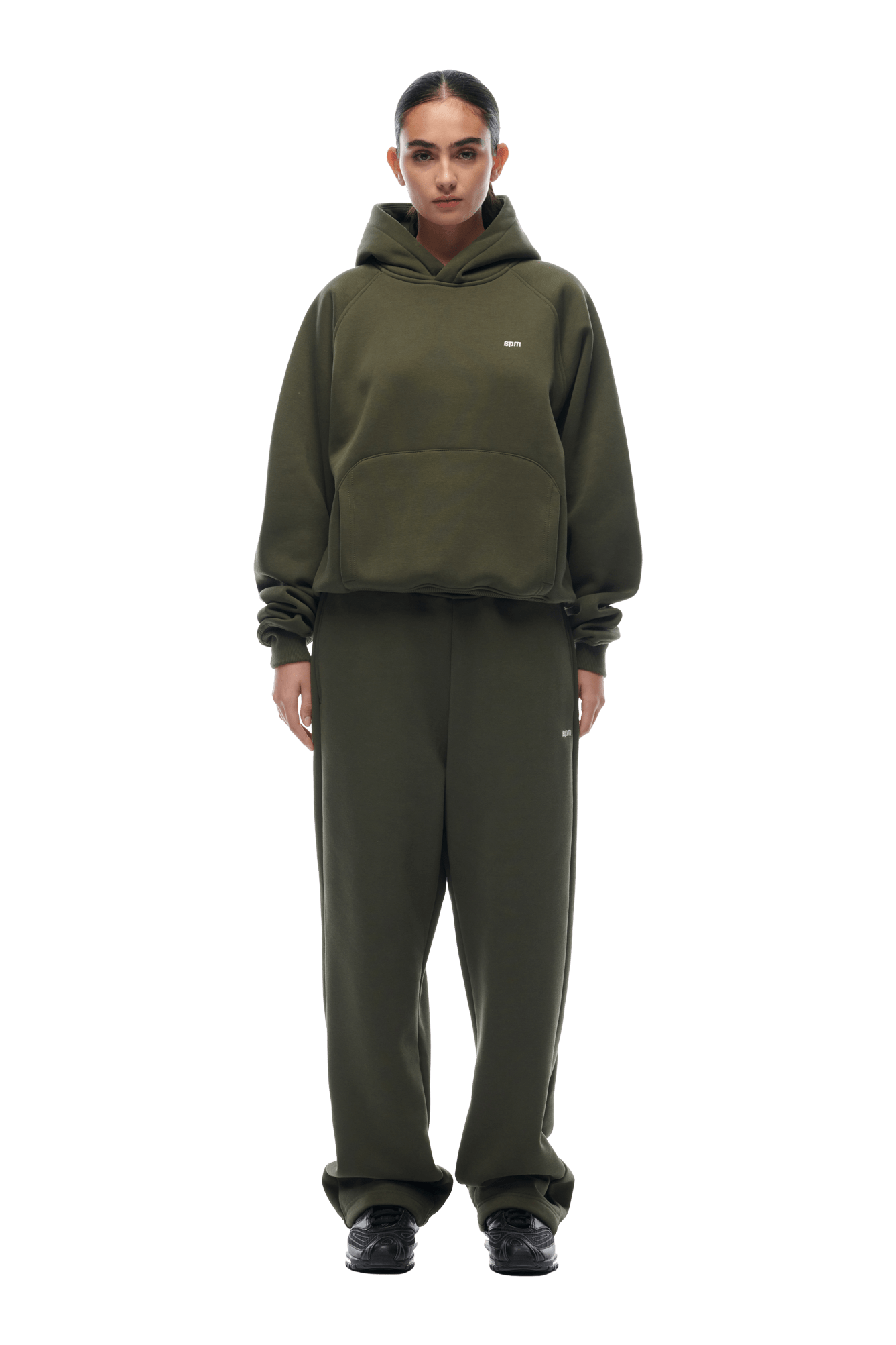 A person faces forward against a plain background, wearing the 6PM HOODIE FOREST NIGHT—a dark green, oversized raglan-sleeved hoodie with matching sweatpants and black sneakers—perfect for everyday wear.