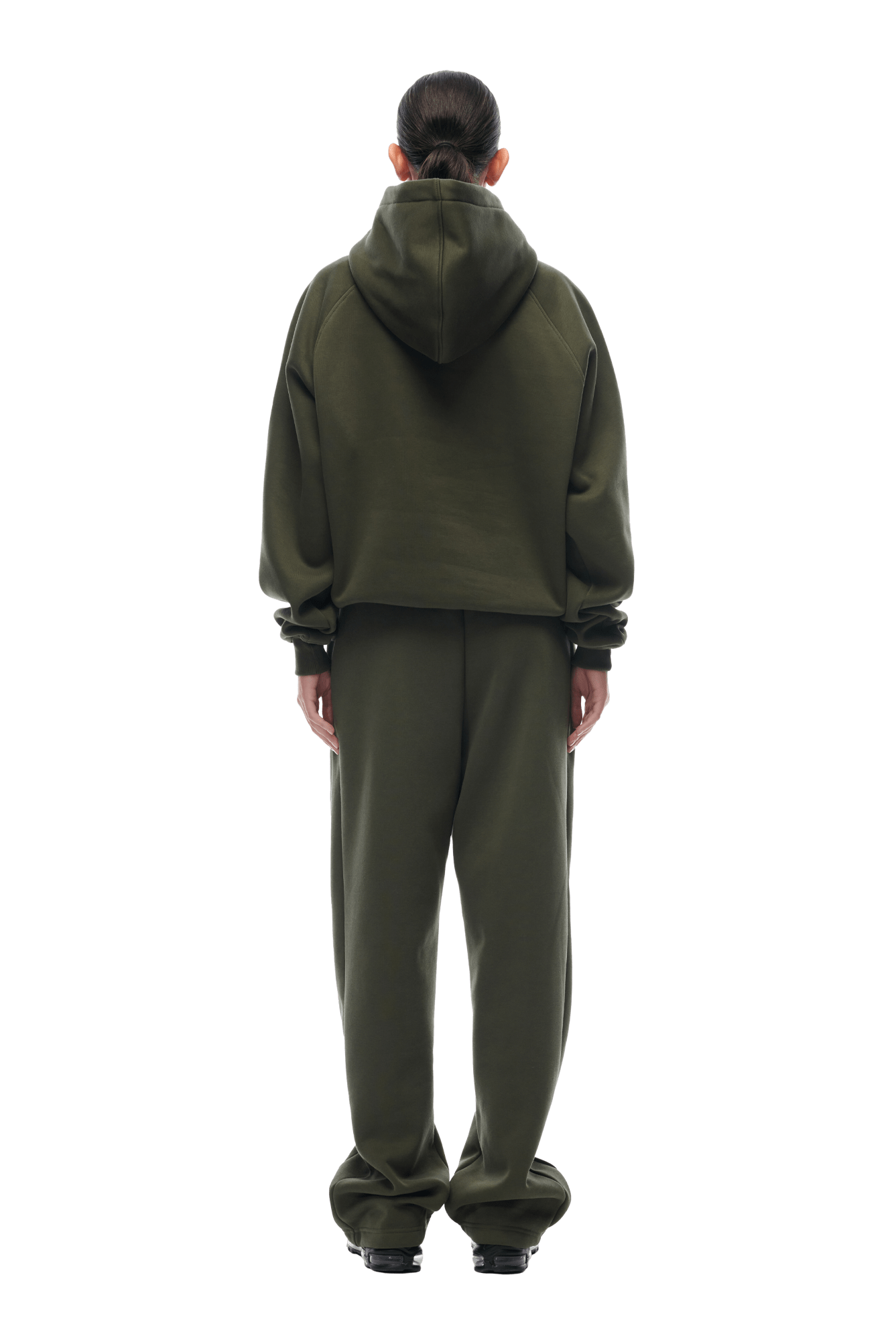 A person stands with their back turned, wearing the 6PM HOODIE FOREST NIGHT and matching loose sweatpants. The oversized hoodie features raglan sleeves and a hood up. Their hair is tied back, black shoes on, with a transparent background.