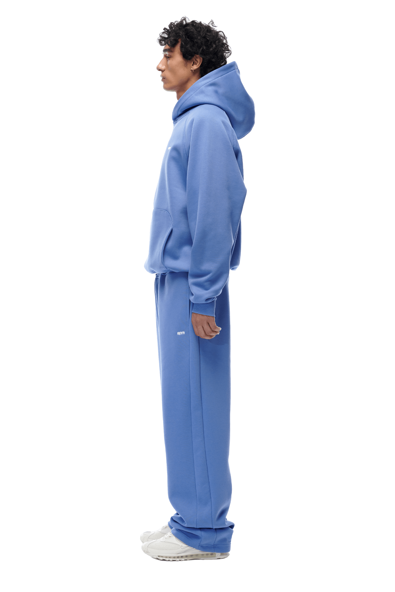 A person in profile wears the 6PM HOODIE PERSIAN BLUE with matching sweatpants and white sneakers, showcasing its raglan sleeves and kangaroo pocket—an ideal everyday outfit against a plain background.