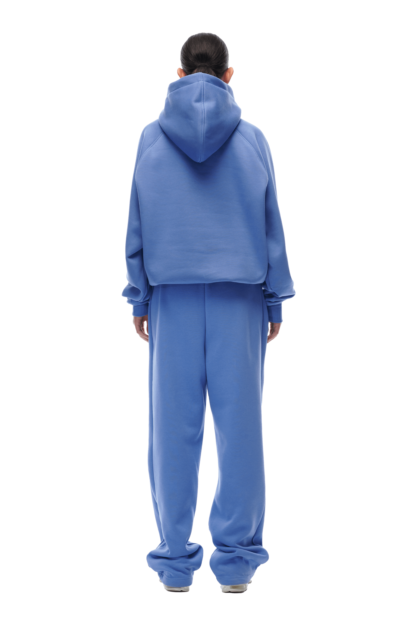 A person stands facing away against a white background, wearing the 6PM HOODIE PERSIAN BLUE with raglan sleeves, the hood up, and matching blue sweatpants. The loose-fit hoodie features a kangaroo pocket and is designed for everyday wear. Hands are by their sides.