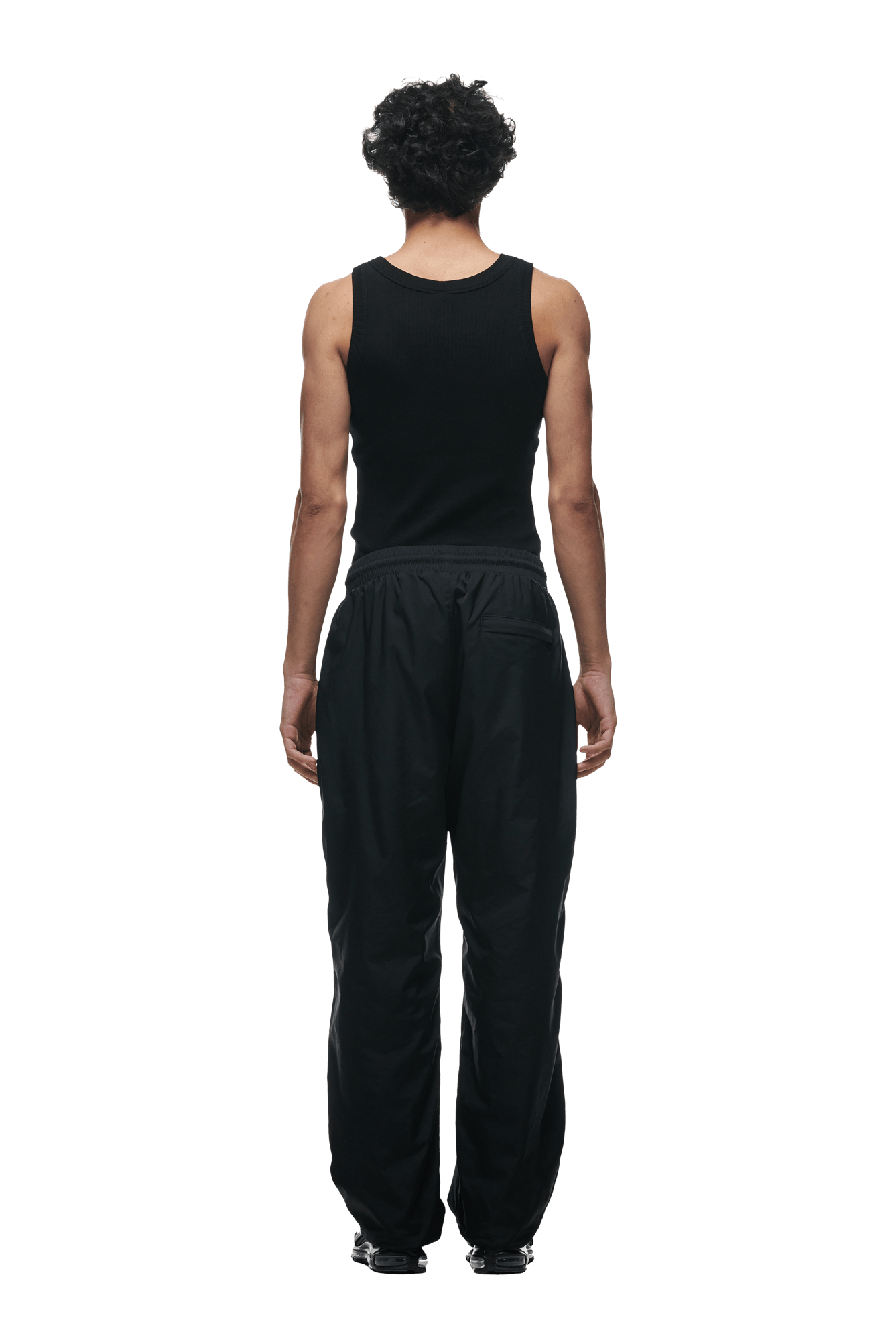 A person with short curly hair, in a black sleeveless top and 6PM 6PM+ NYLON PANTS OPEN LEG BLACK, stands facing away from the camera against a plain green background.