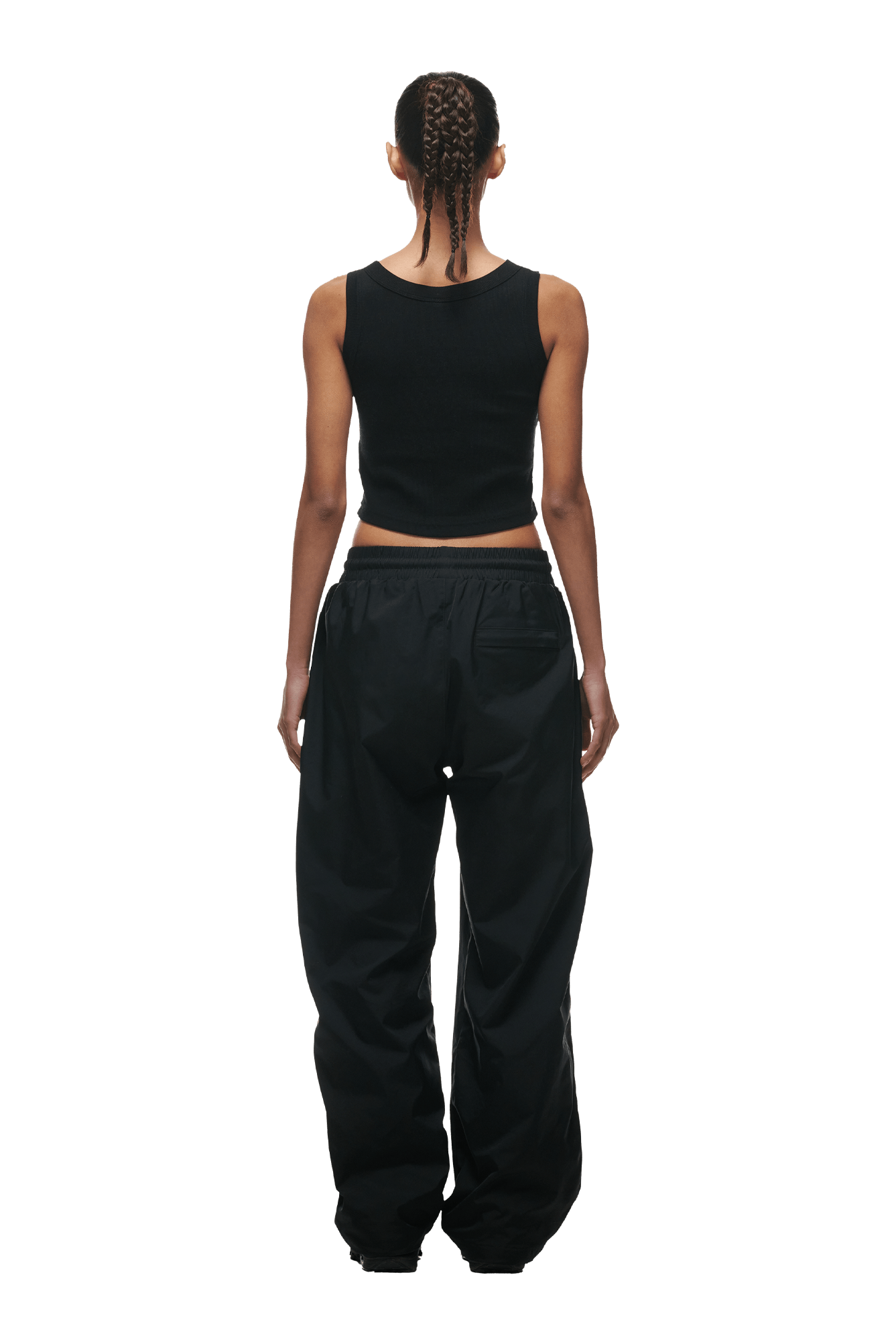 A person with braided hair faces away from the camera, wearing a black sleeveless crop top and 6PM+ NYLON PANTS OPEN LEG BLACK by 6PM, featuring loose fit and zipped pockets, set against a plain background.
