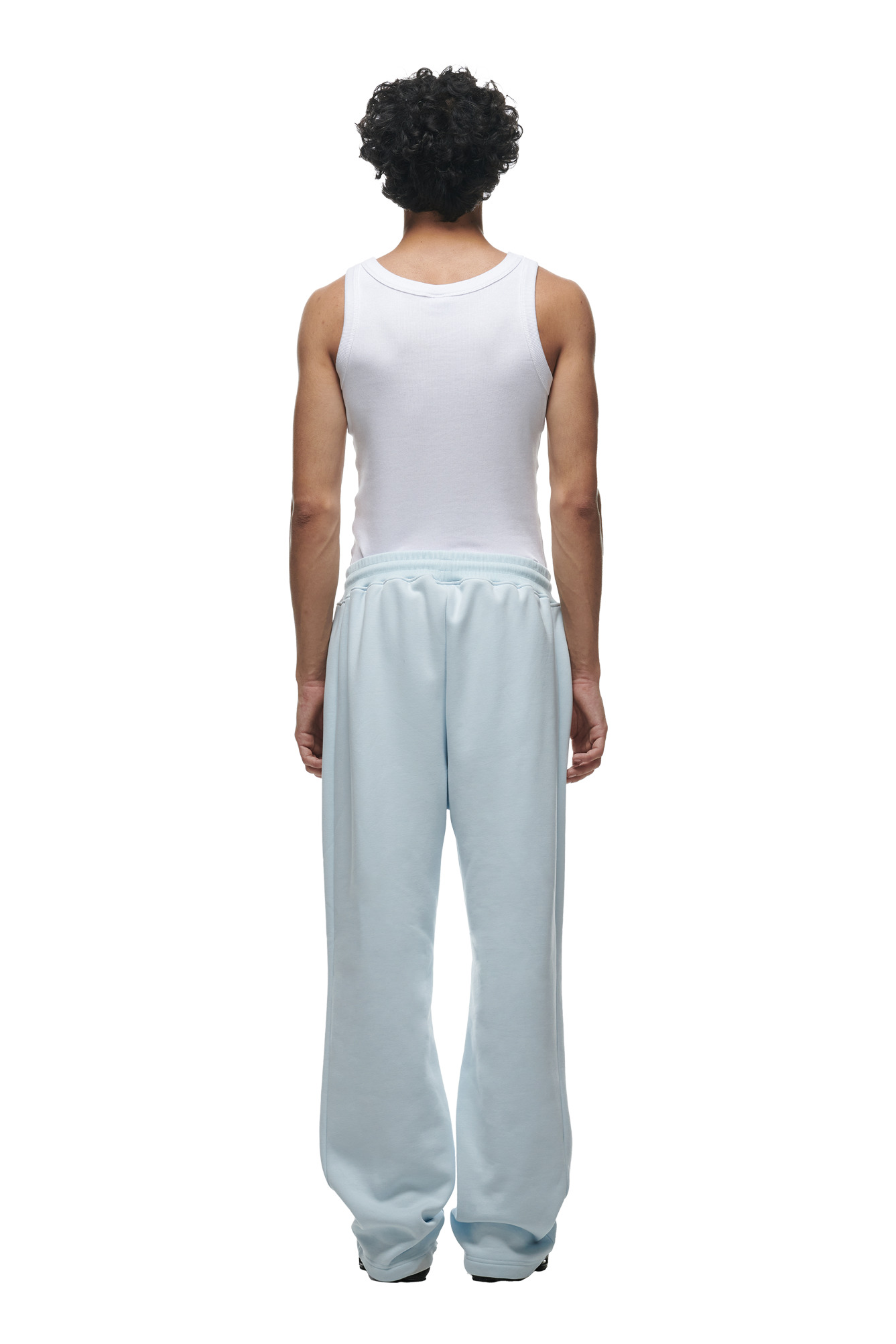 A person with curly hair faces away from the camera, wearing a white tank top and 6PM’s OPEN LEG JOGGER ICE BLUE sweatpants for a modern classic look.