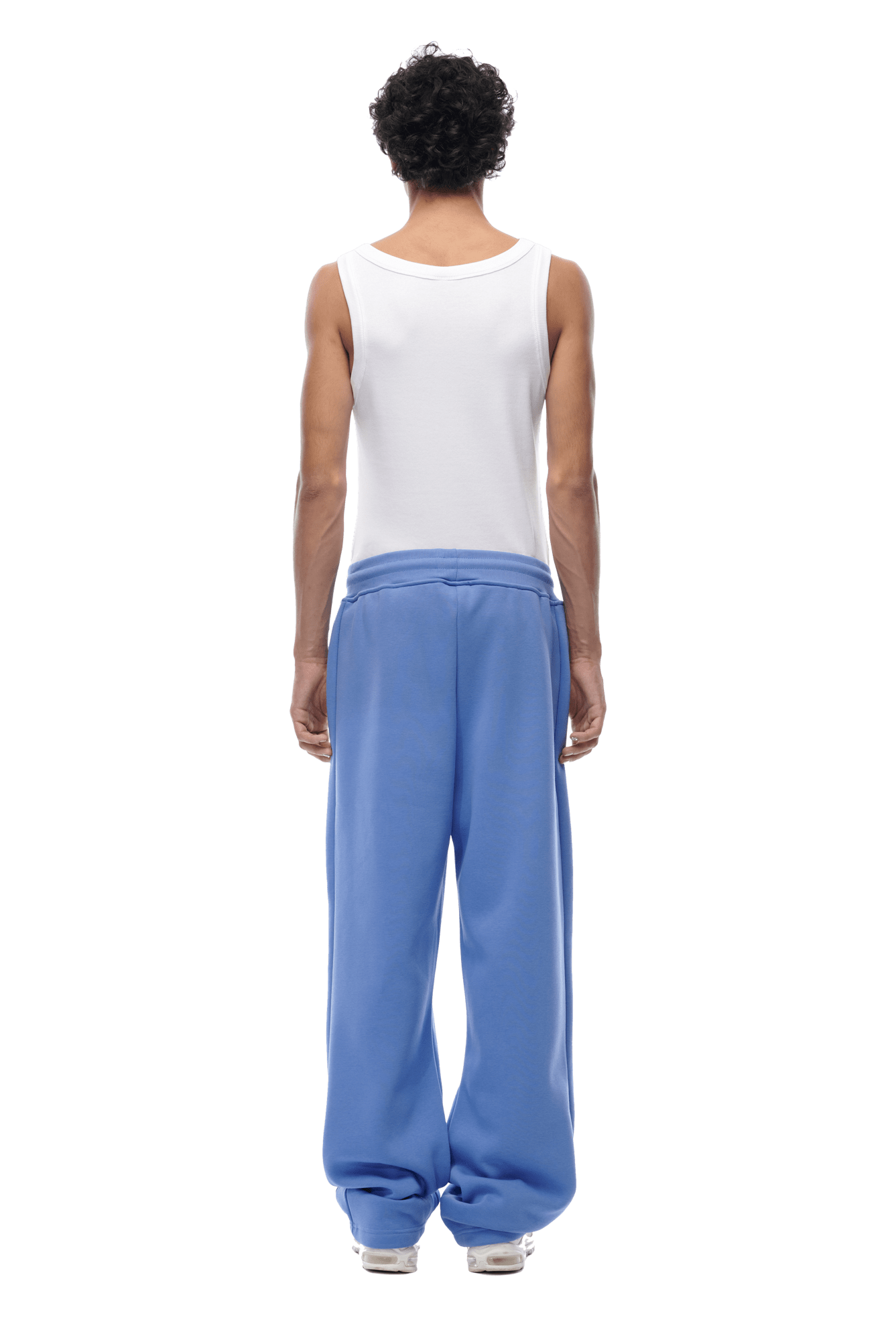 A person with short curly hair wears a white tank top and 6PMs OPEN LEG JOGGER PERSIAN BLUE, standing with their back to the camera against a transparent background for a modern classic look.