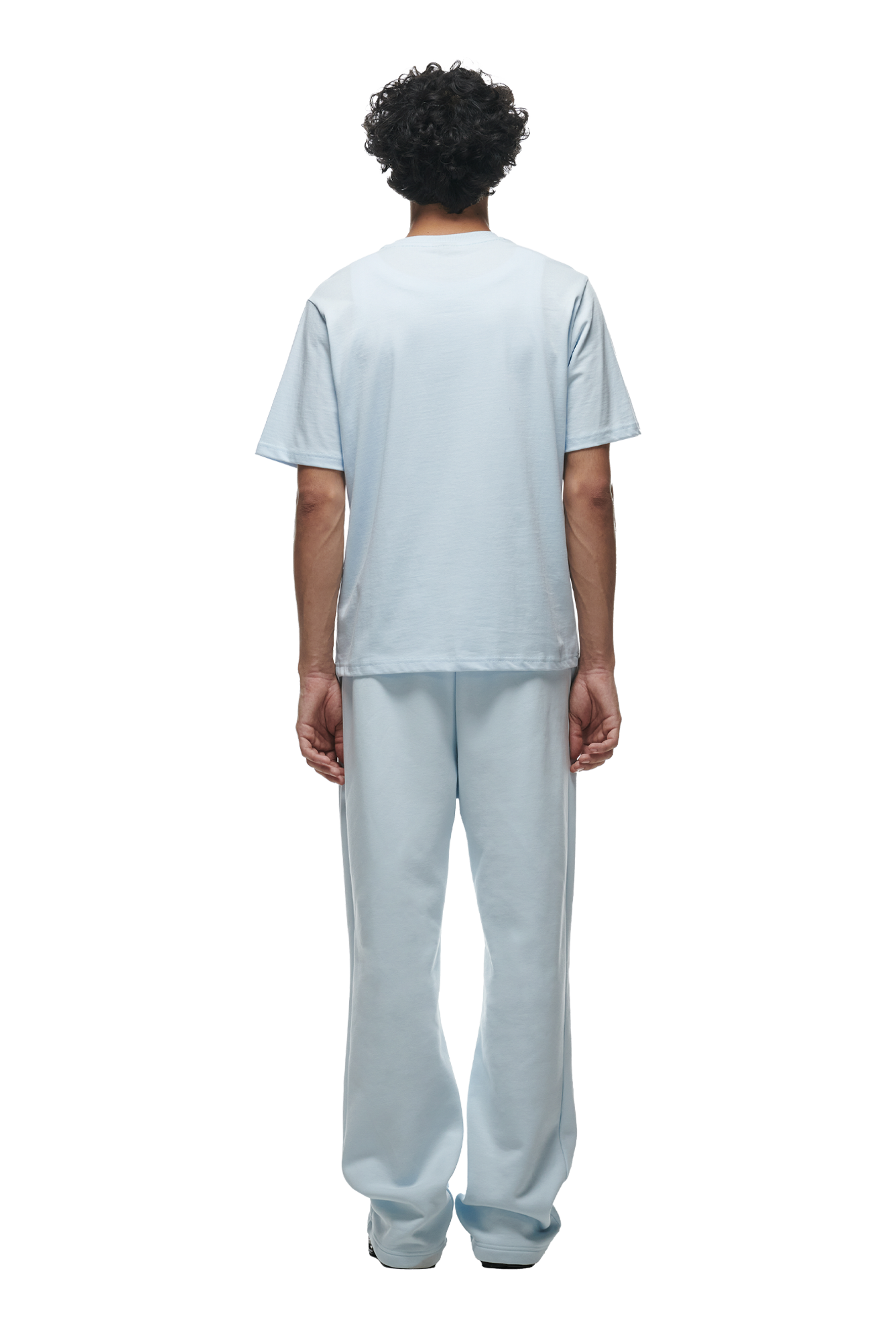 A person with curly hair is standing and facing away from the camera, wearing the 6PM T-SHIRT ICE BLUE with matching light blue pants.