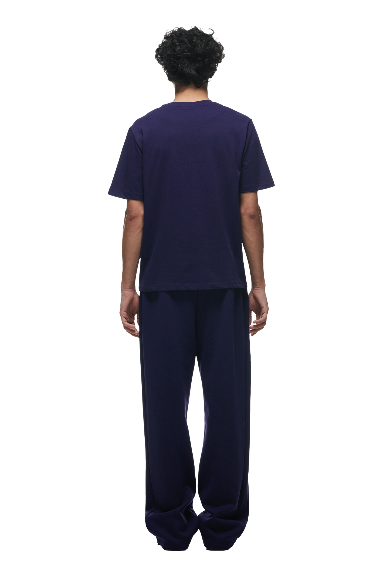 A person with short curly hair stands facing away, wearing the 6PM T-SHIRT ORBIT BLUE and matching wide-legged pants against a white background.