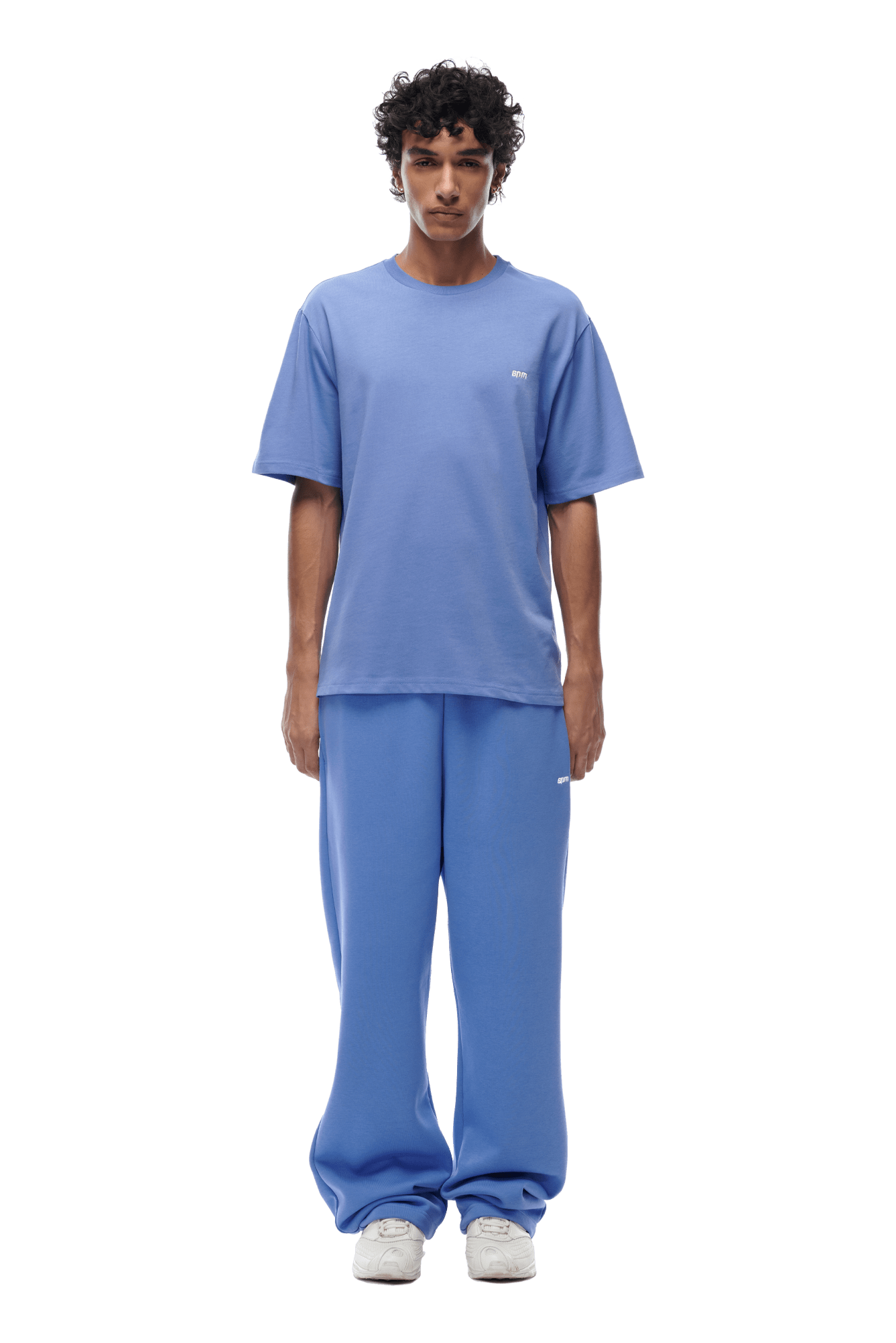 A person stands facing forward, wearing the 6PM T-SHIRT PERSIAN BLUE and matching blue sweatpants with white sneakers, against a plain background.