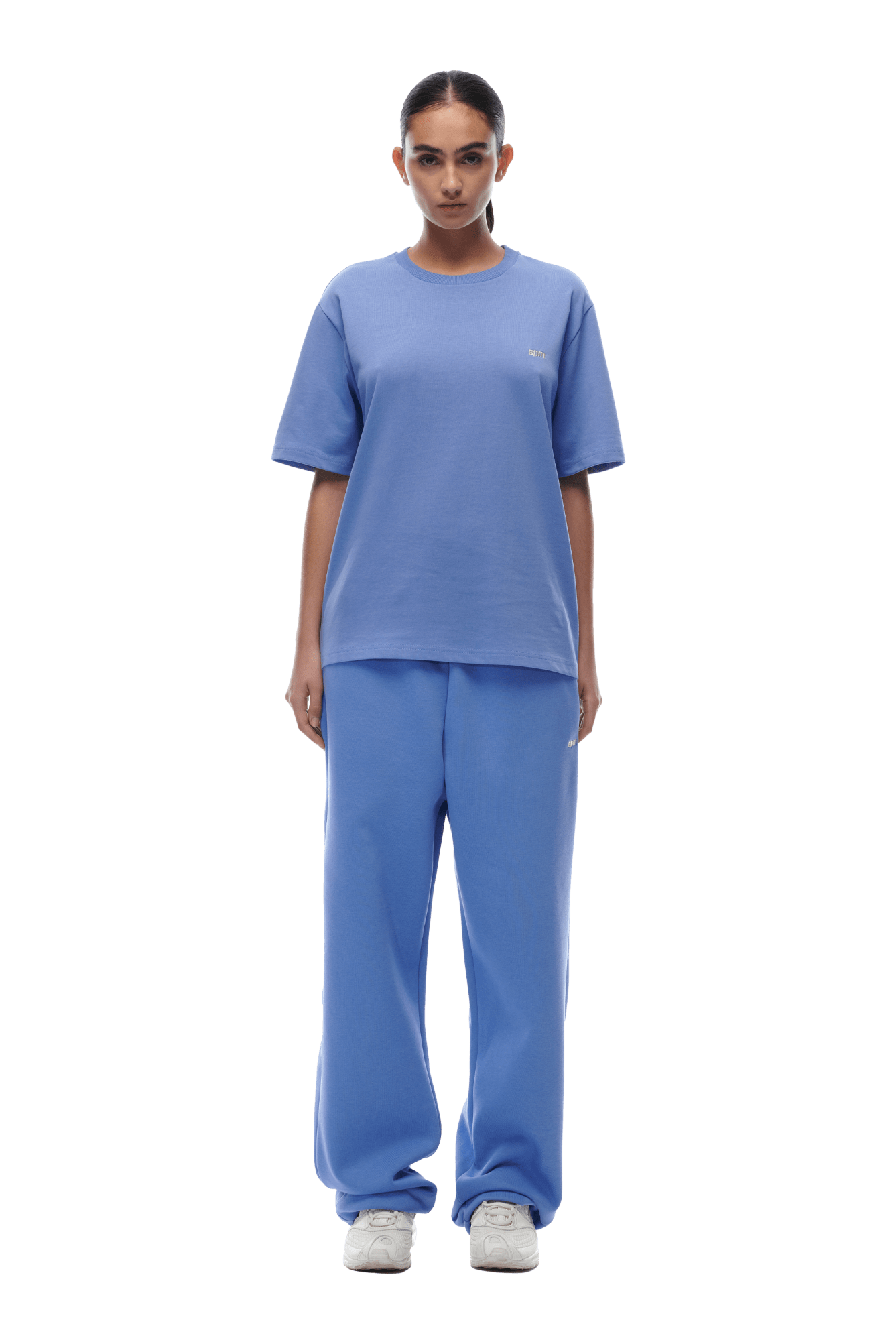 A person stands facing forward, wearing the 6PM T-SHIRT PERSIAN BLUE with matching sweatpants and white sneakers, set against a transparent background.