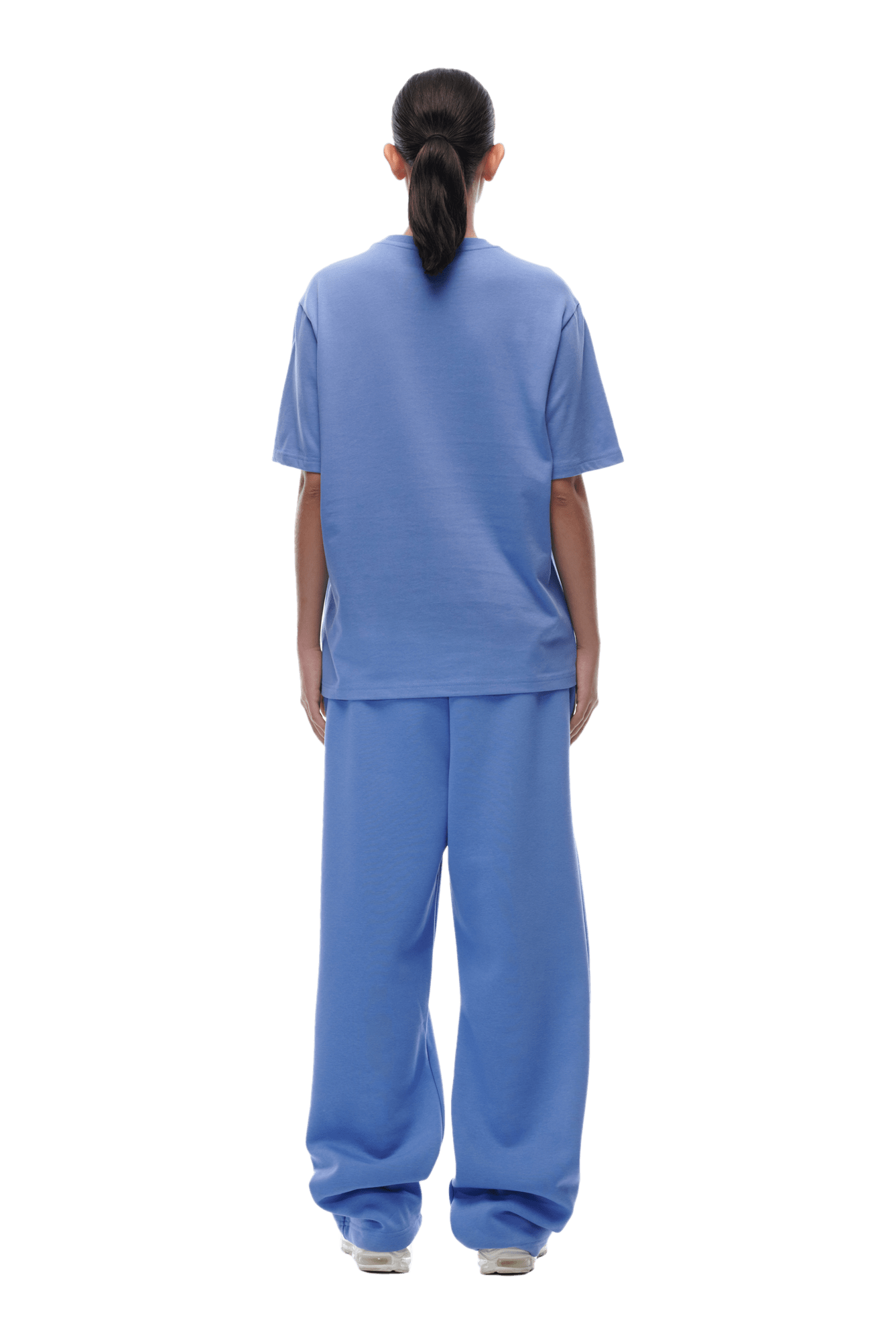 A person with long dark hair in a ponytail wears the 6PM T-SHIRT PERSIAN BLUE and matching wide blue pants, standing facing away from the camera against a transparent background.