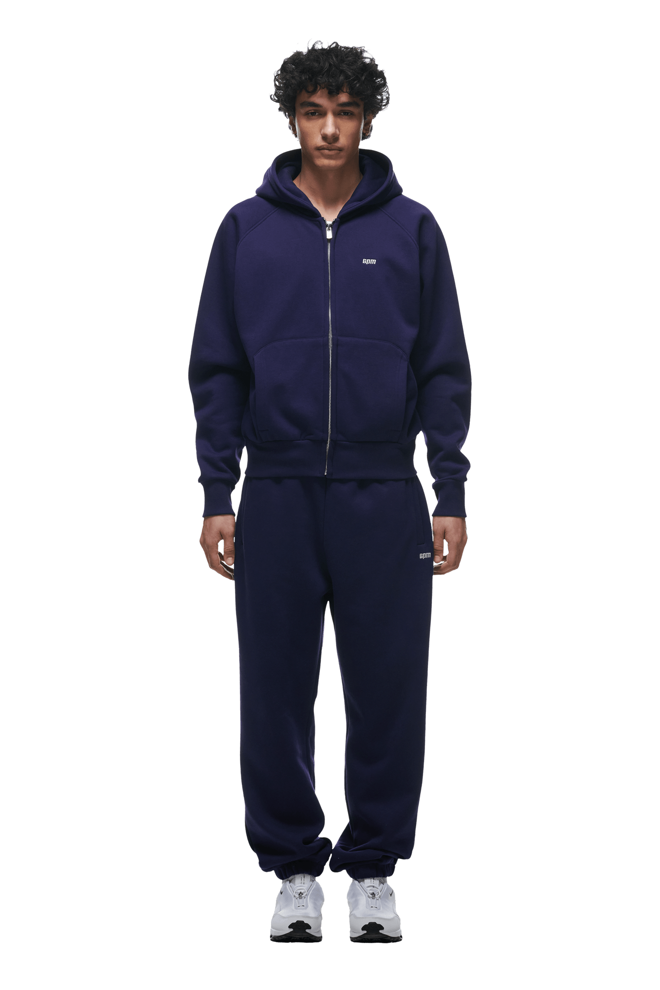 A man faces forward in a matching 6PM ZIP HOODIE ORBIT BLUE set, paired with white sneakers. The outfit offers a clean, versatile look ideal for daily wear. Transparent background.