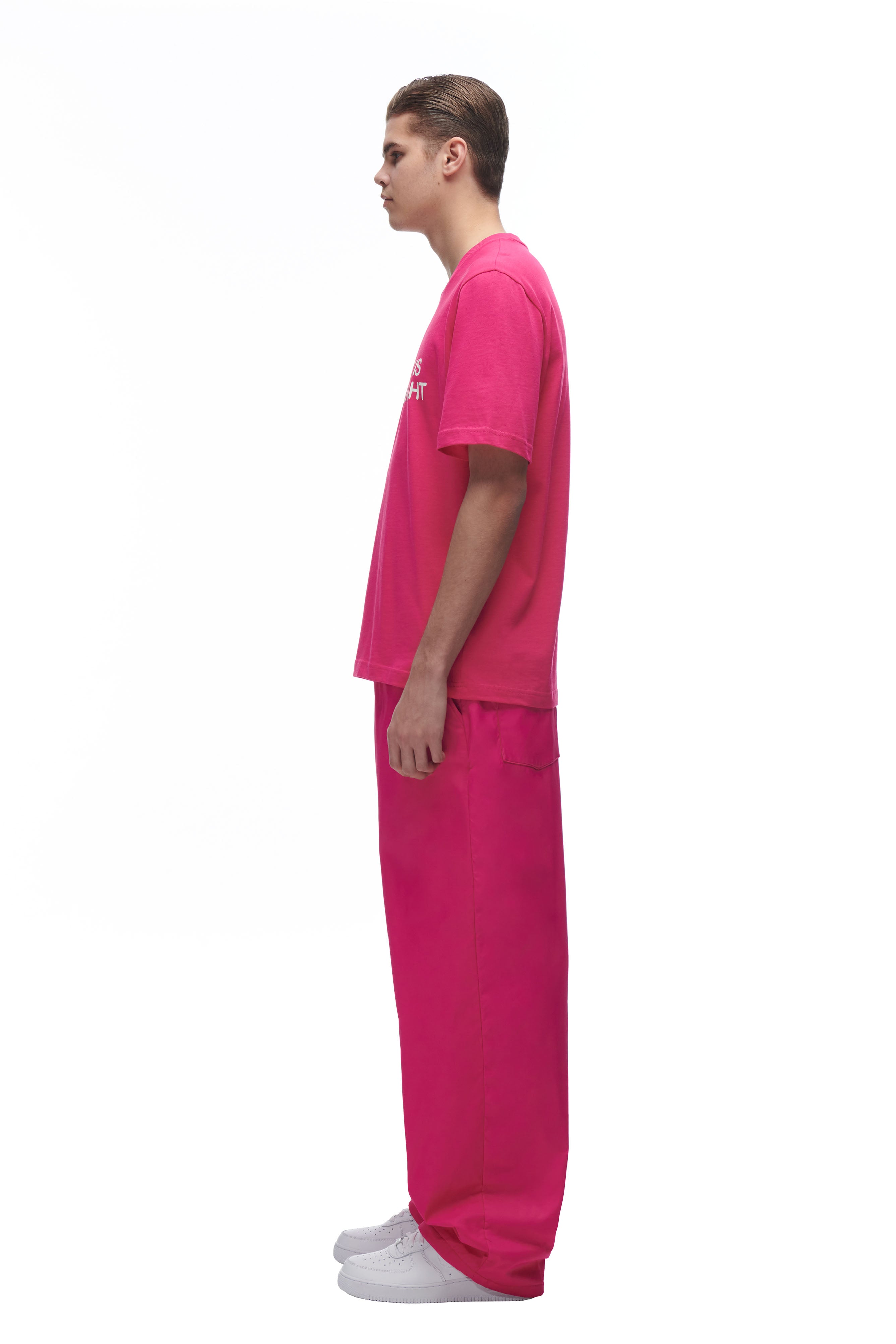 A person stands in profile against a white background, wearing the 6PM DATENIGHT T-SHIRT PINK with matching wide-leg pants and white sneakers.