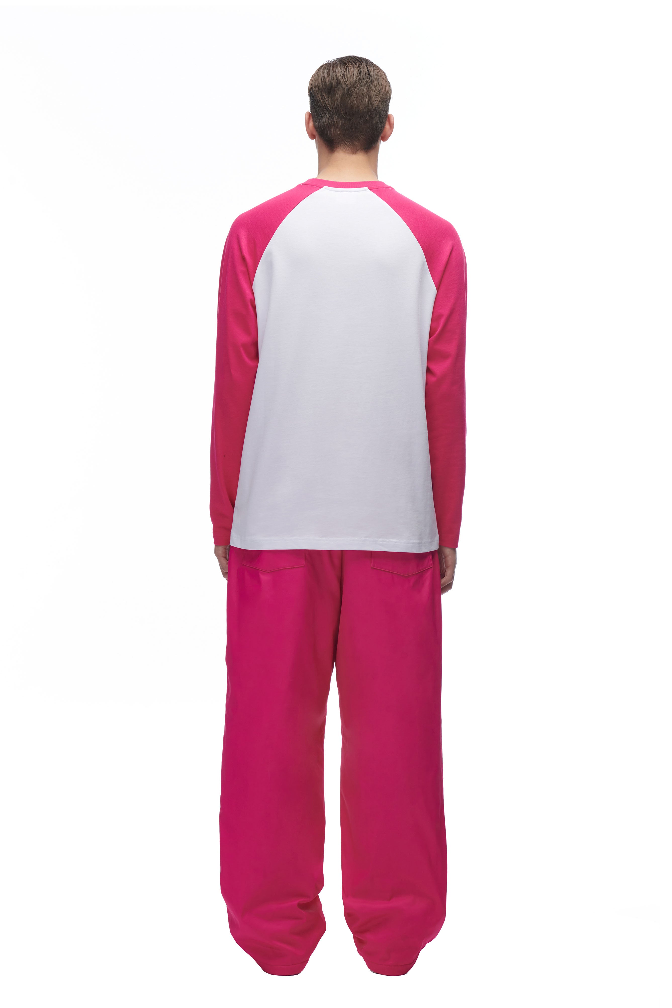 A person stands with their back to the camera, wearing the 6PM LH LONGSLEEVE WHITE/PINK top and loose, bright pink pants, set against a plain white background.
