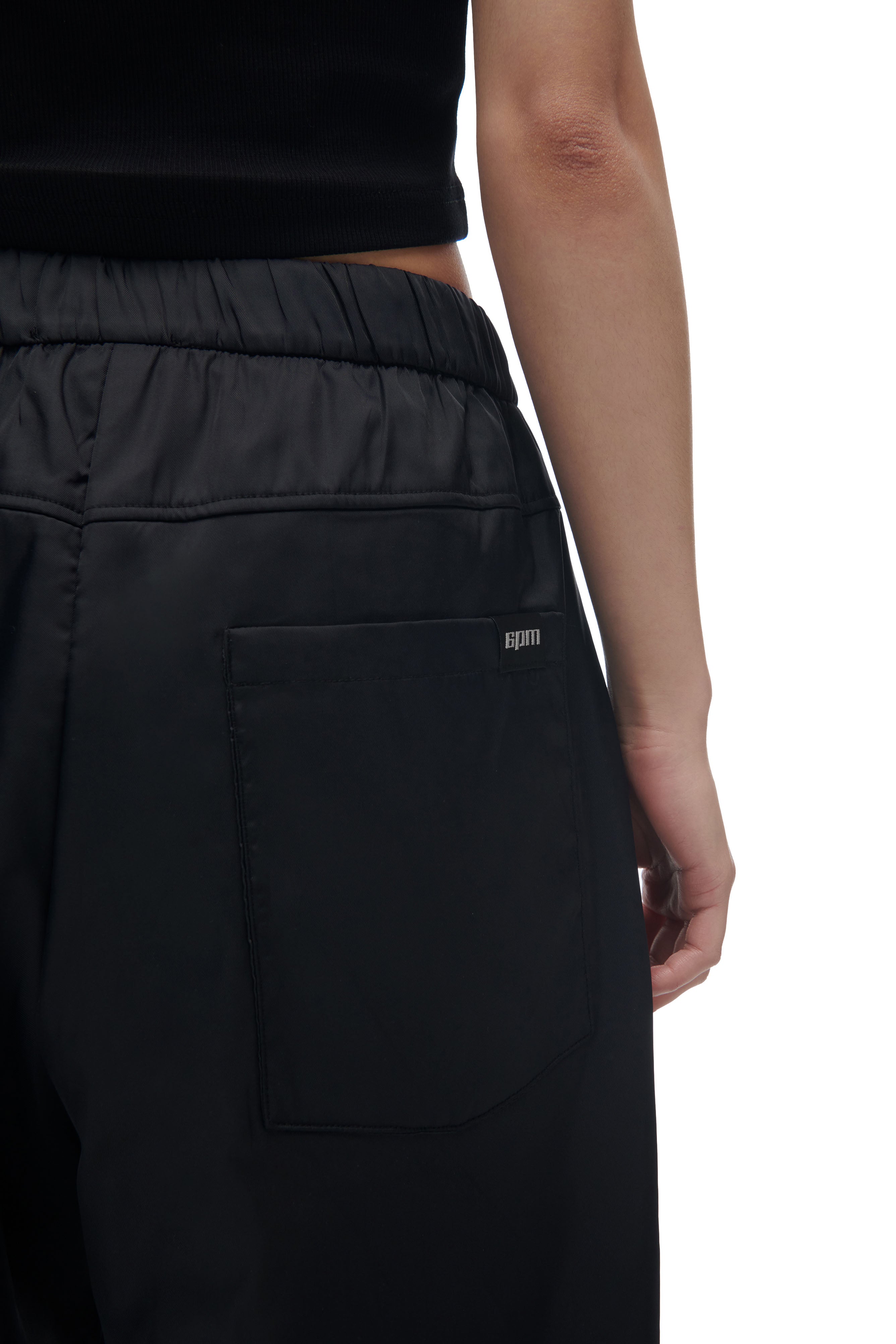 A person is shown from the back and side wearing 6PM’s LH NYLON PANTS BLACK, highlighting the pocket's small gpm logo. The background is white.