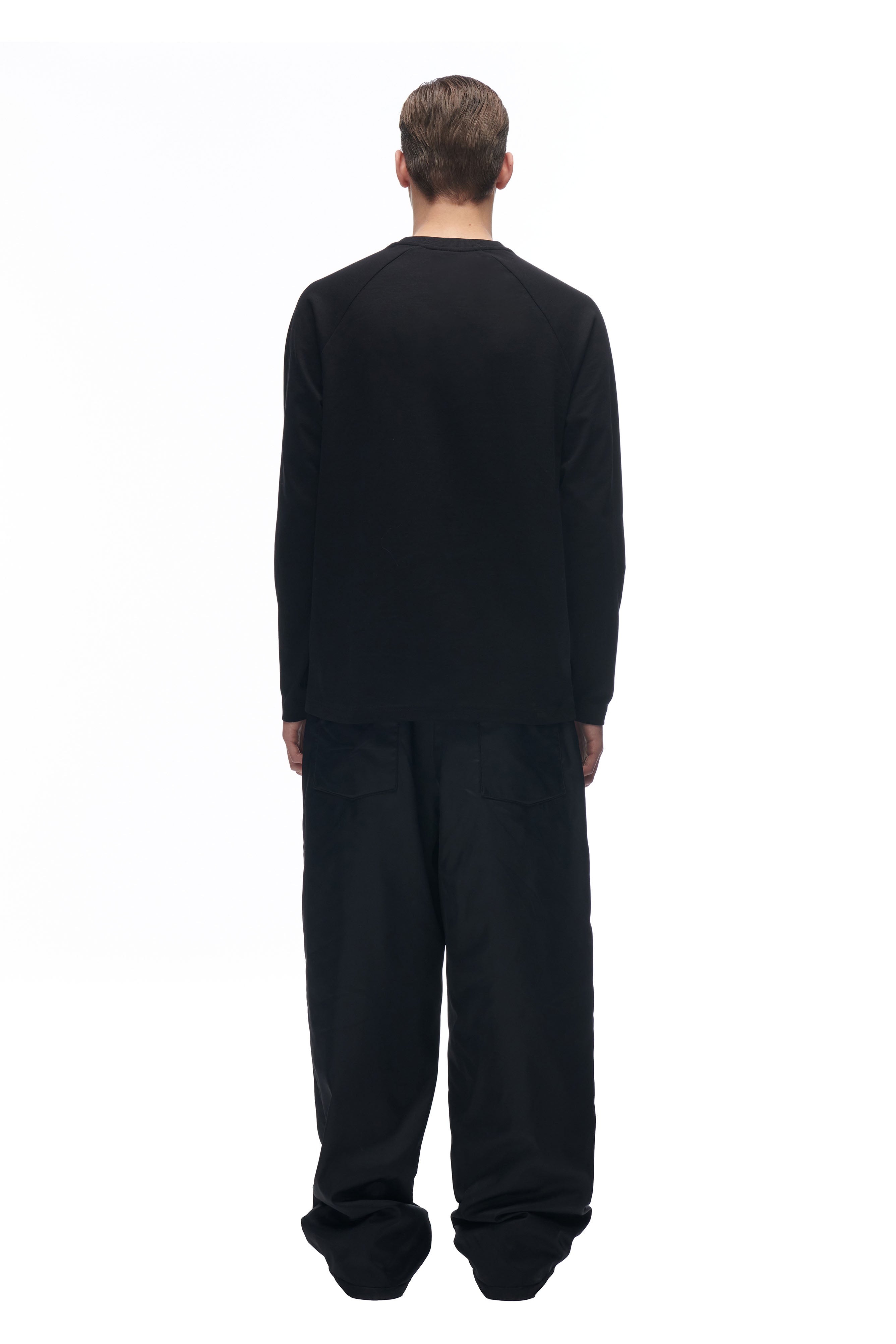 A person stands with their back to the camera, modeling the 6PM LH LONGSLEEVE BLACK/BLACK shirt and loose black pants against a plain white background.