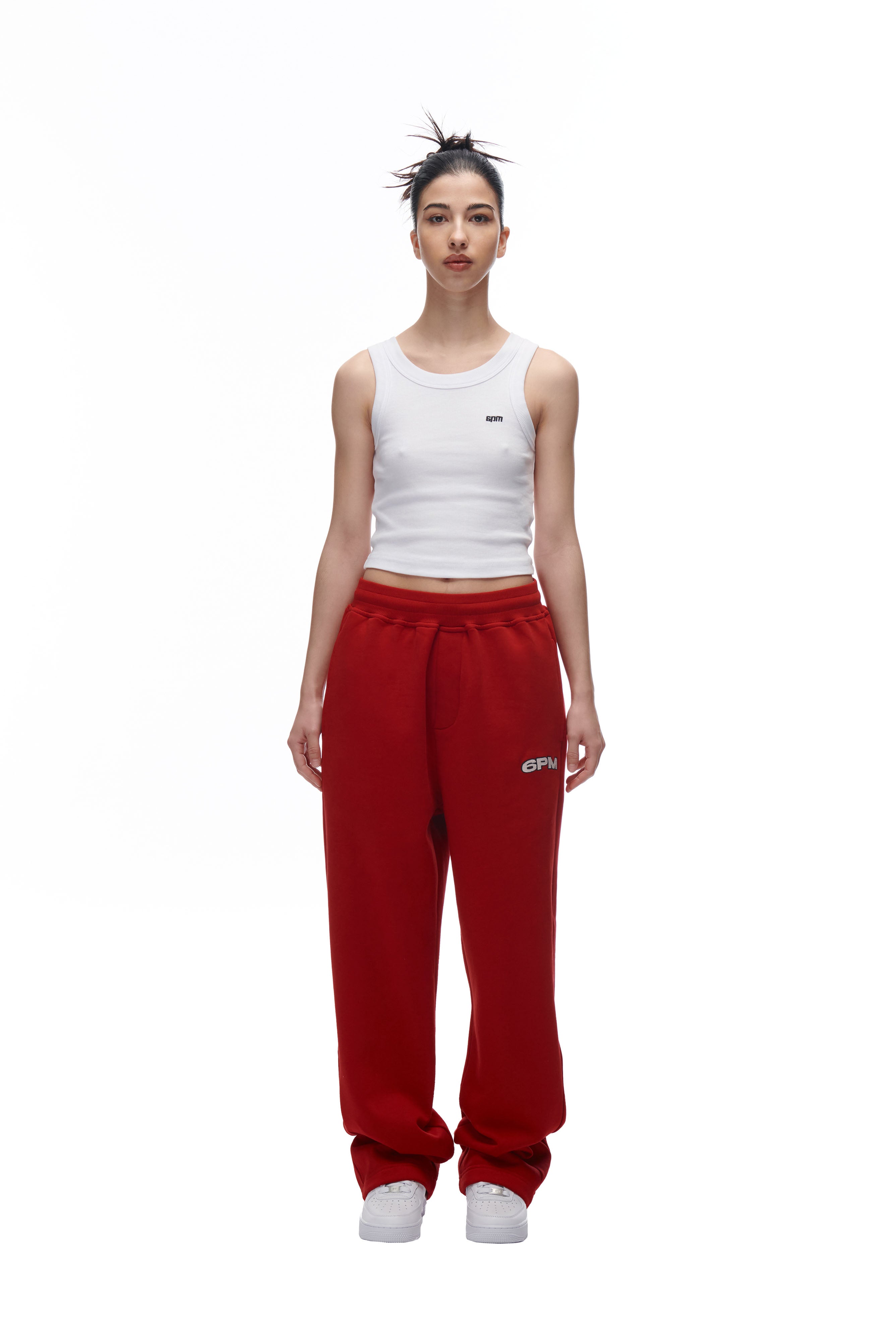 A person stands facing forward on a plain white background, wearing a white tank top and 6PM LH SWEATPANT RED with white sneakers. Both the tank top and sweatpants feature a small 6PM logo.